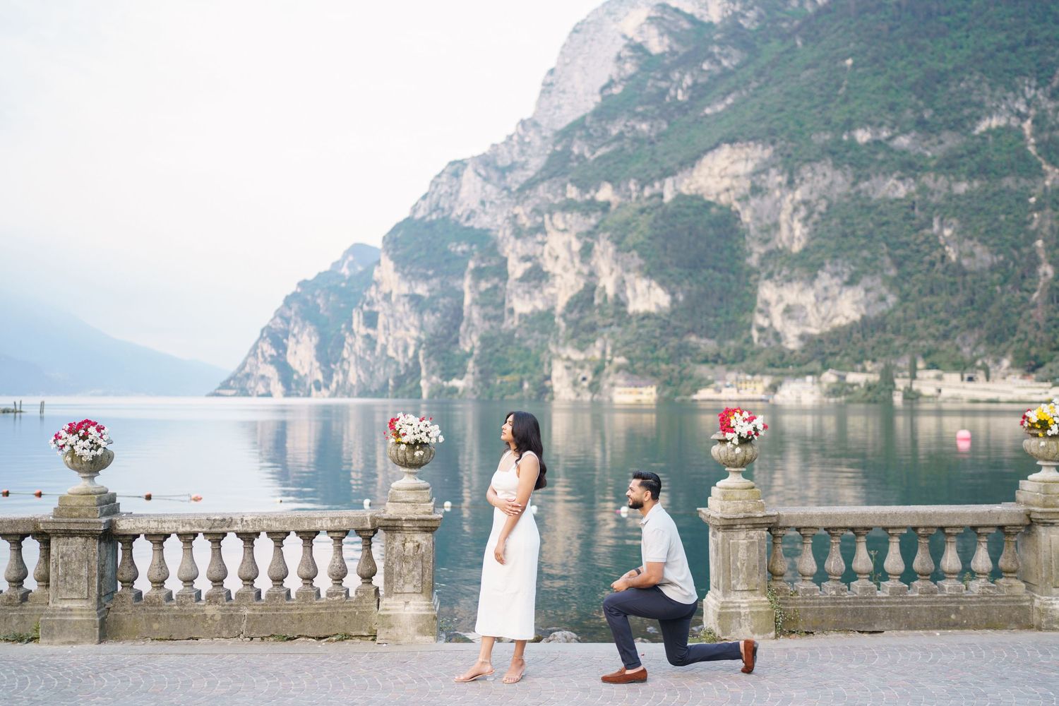 A romantic proposal moment on a stone balcony overlooking Lake Garda in Italy with dramatic mountain scenery.