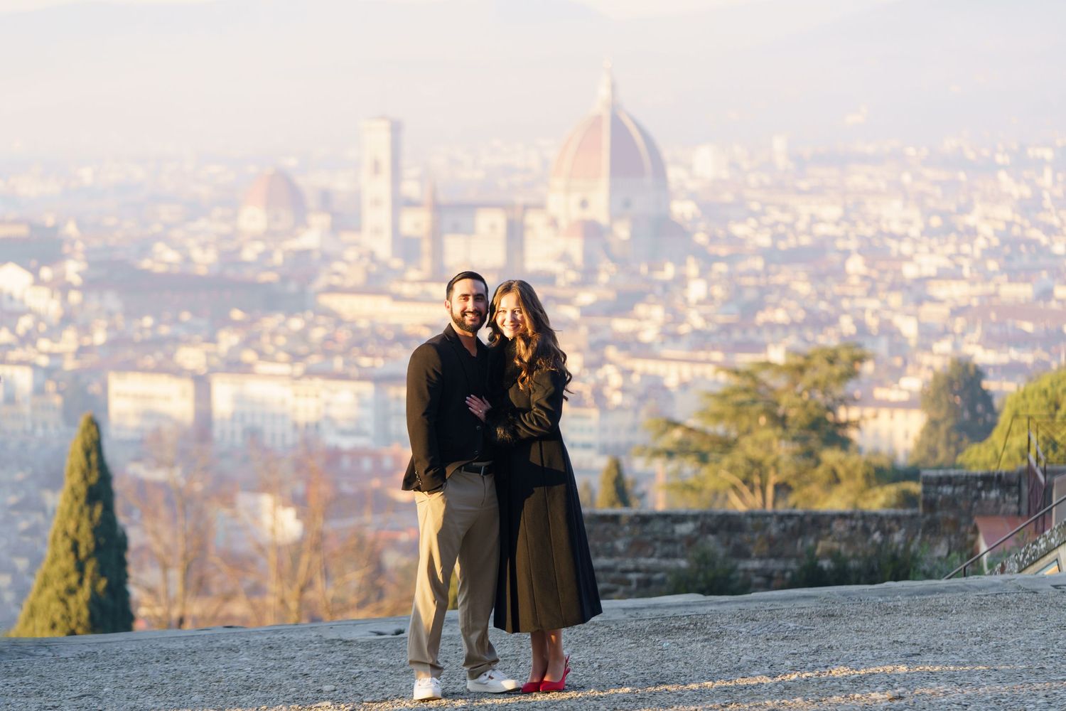 Couple enjoying scenic view of Florence cityscape with Duomo cathedral from Piazzale Michelangelo at sunset.