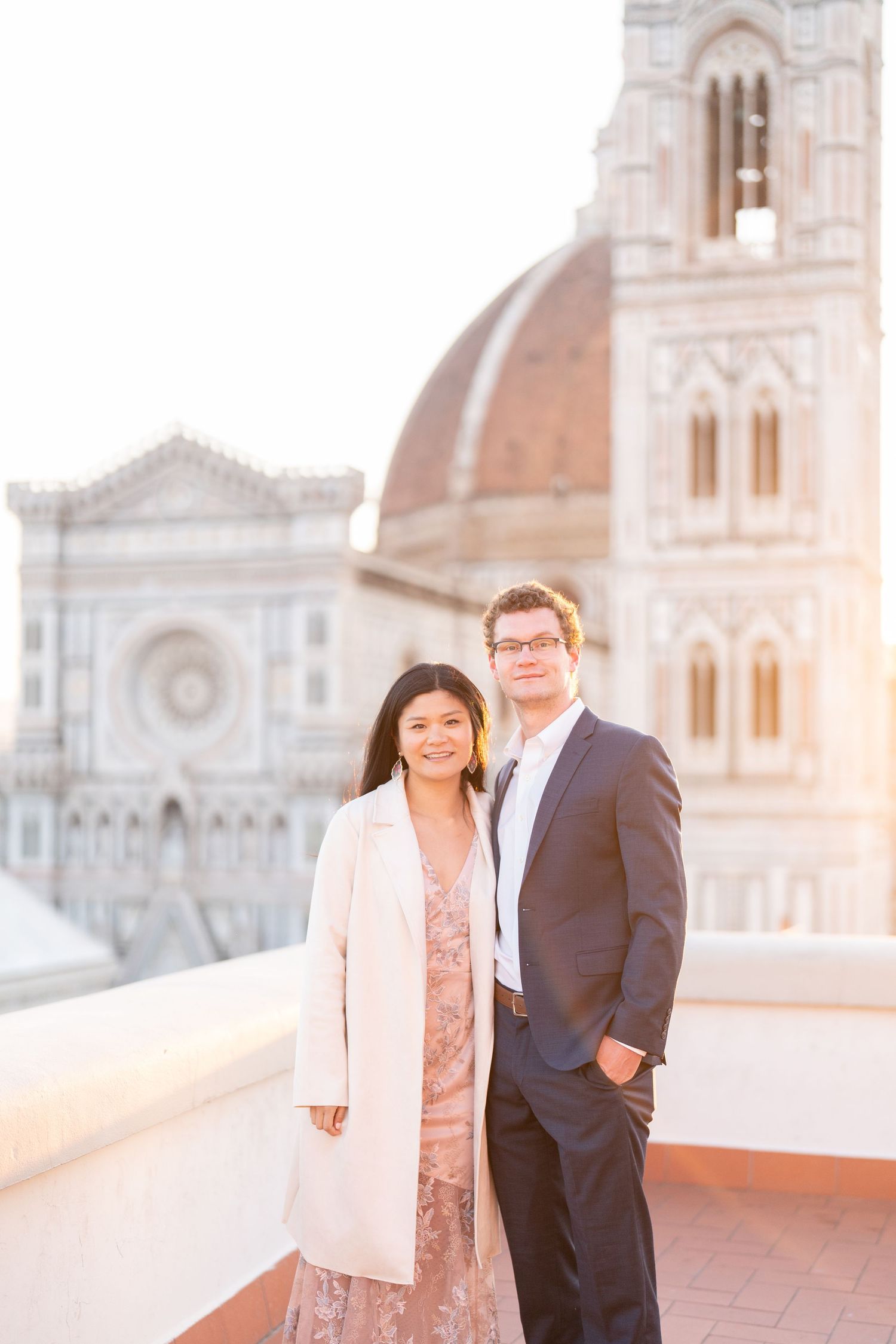 Couple posing together on a rooftop terrace with Florence Cathedral and historic Italian architecture in background.