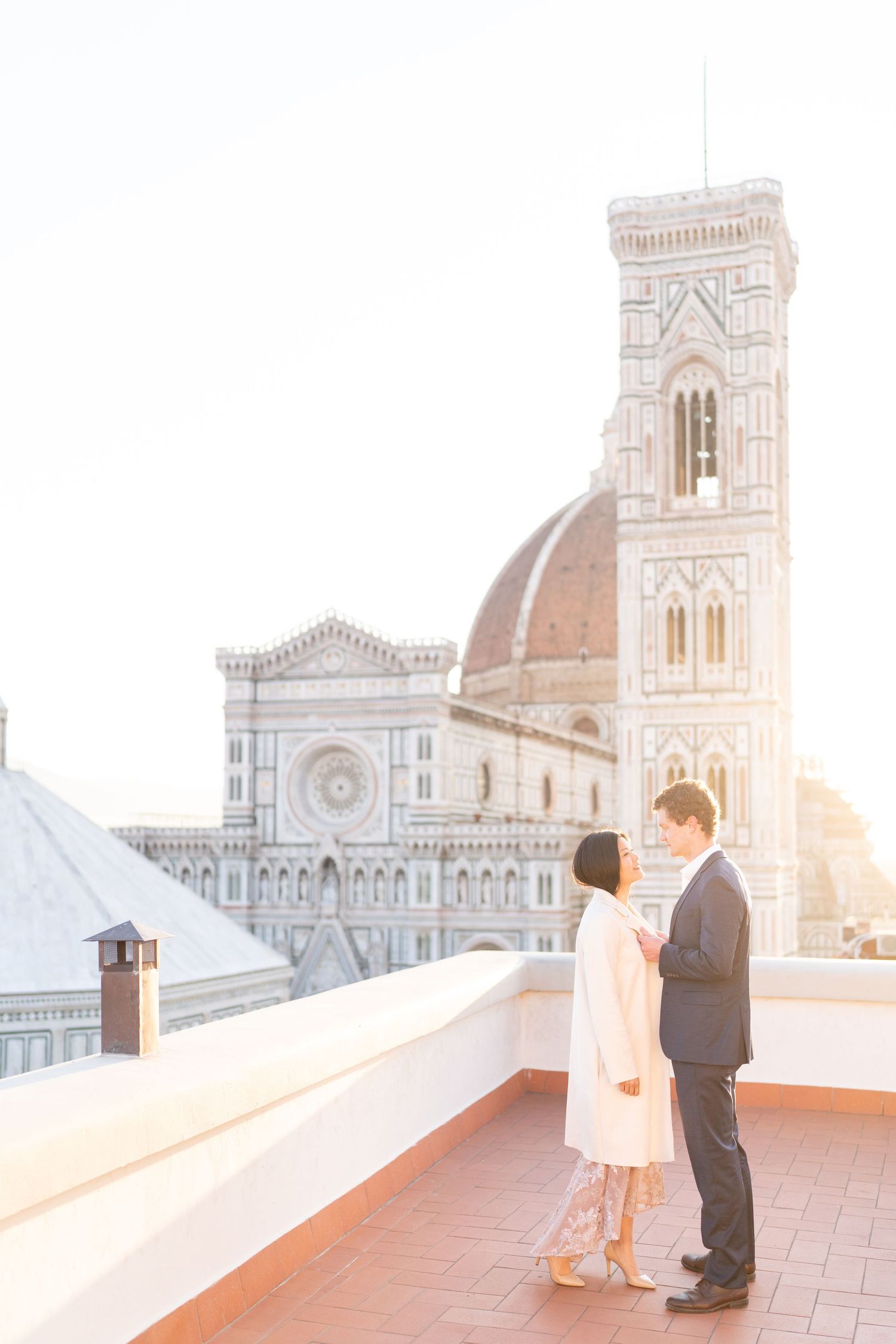 A couple stands on a rooftop terrace overlooking the historic Duomo cathedral in Florence, Italy during sunset.
