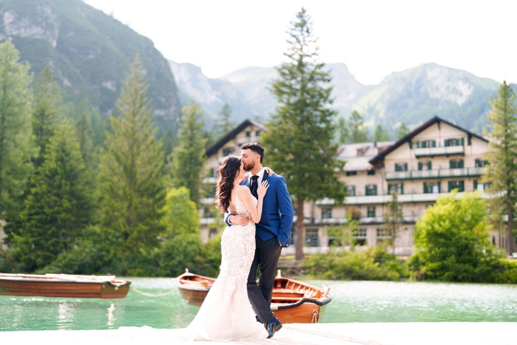 Romantic wedding moment captured by a mountain lake with wooden boats and alpine scenery.