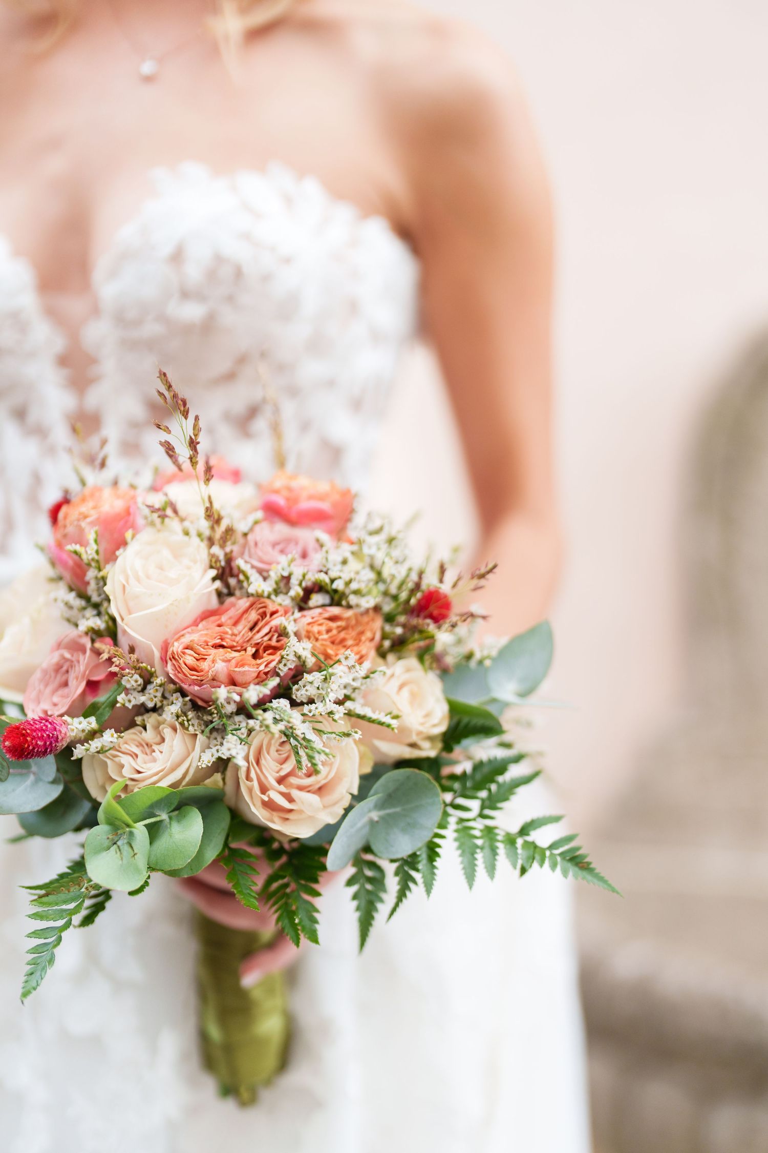 Bridal bouquet with peach and coral roses, eucalyptus leaves, and greenery against white dress.