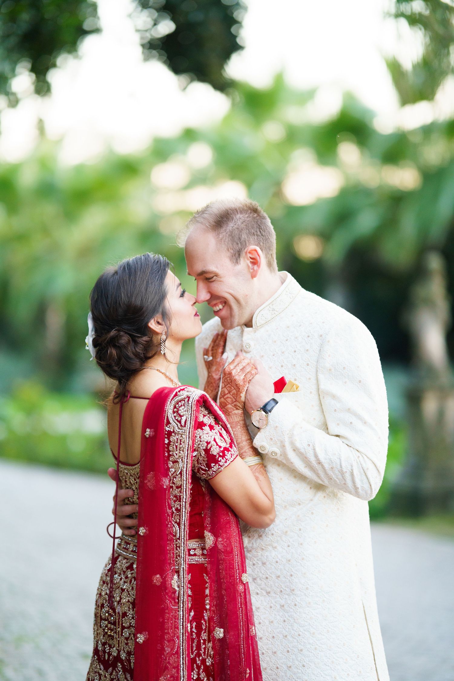 A romantic moment between a couple in traditional fusion wedding attire surrounded by greenery.