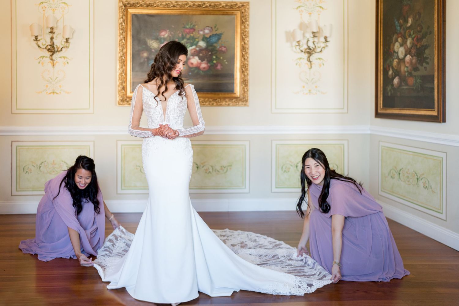 Elegant wedding party photo session in ornate room with white walls and gold-framed artwork.
