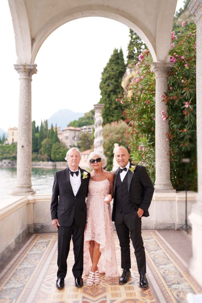 Formal gathering on a lakeside terrace with classical Italian architecture and mountain views.
