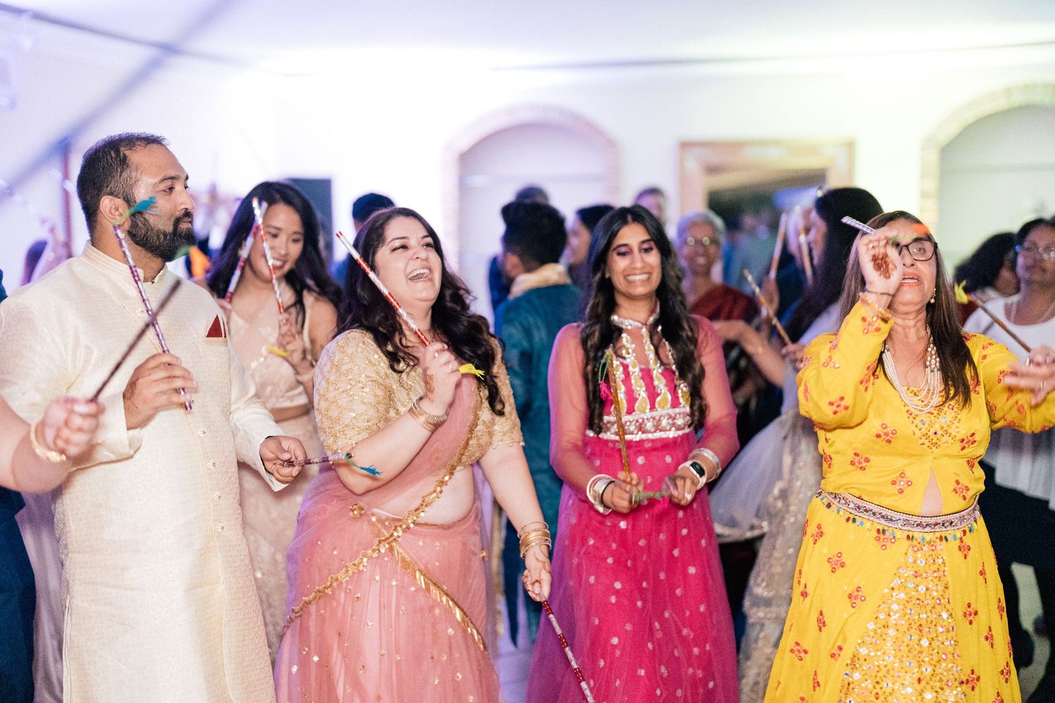Wedding guests in bright traditional dresses dance together during a festive celebration.