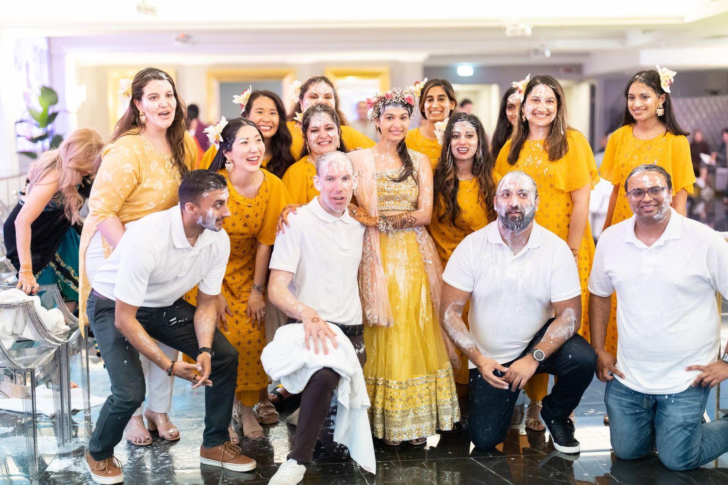 Large group in white shirts and yellow outfits posing together at an indoor celebration.