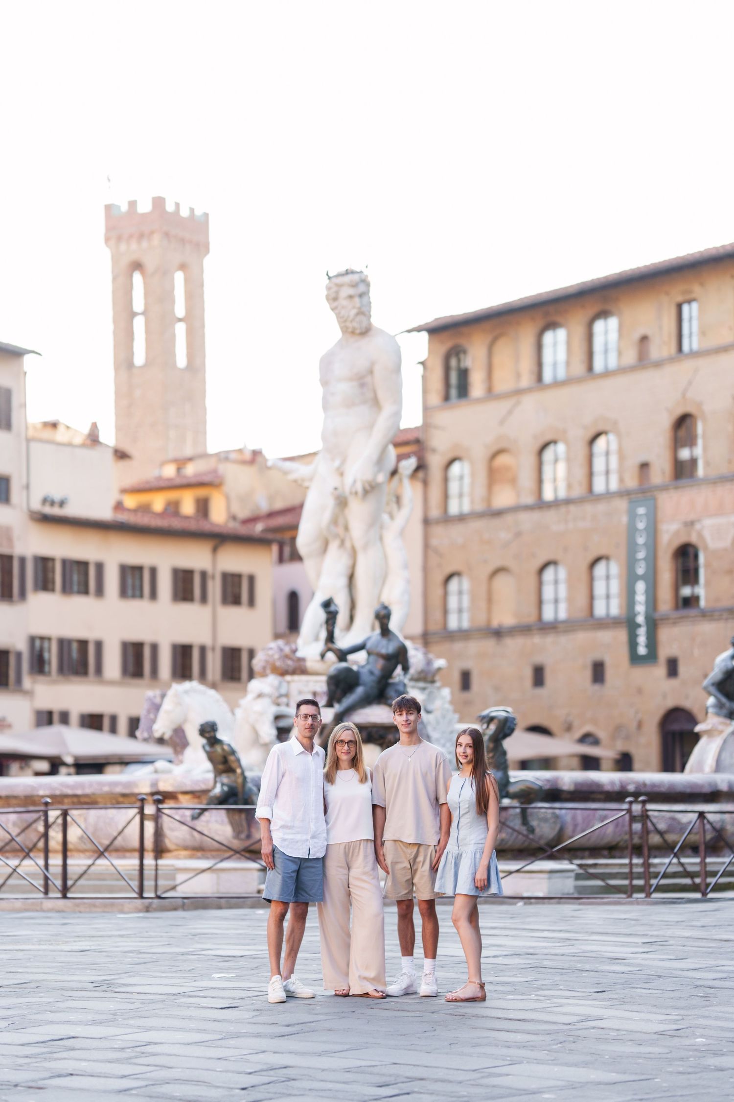 Tourists admiring Neptune Fountain in Piazza della Signoria, Florence with historic architecture and tower in background.