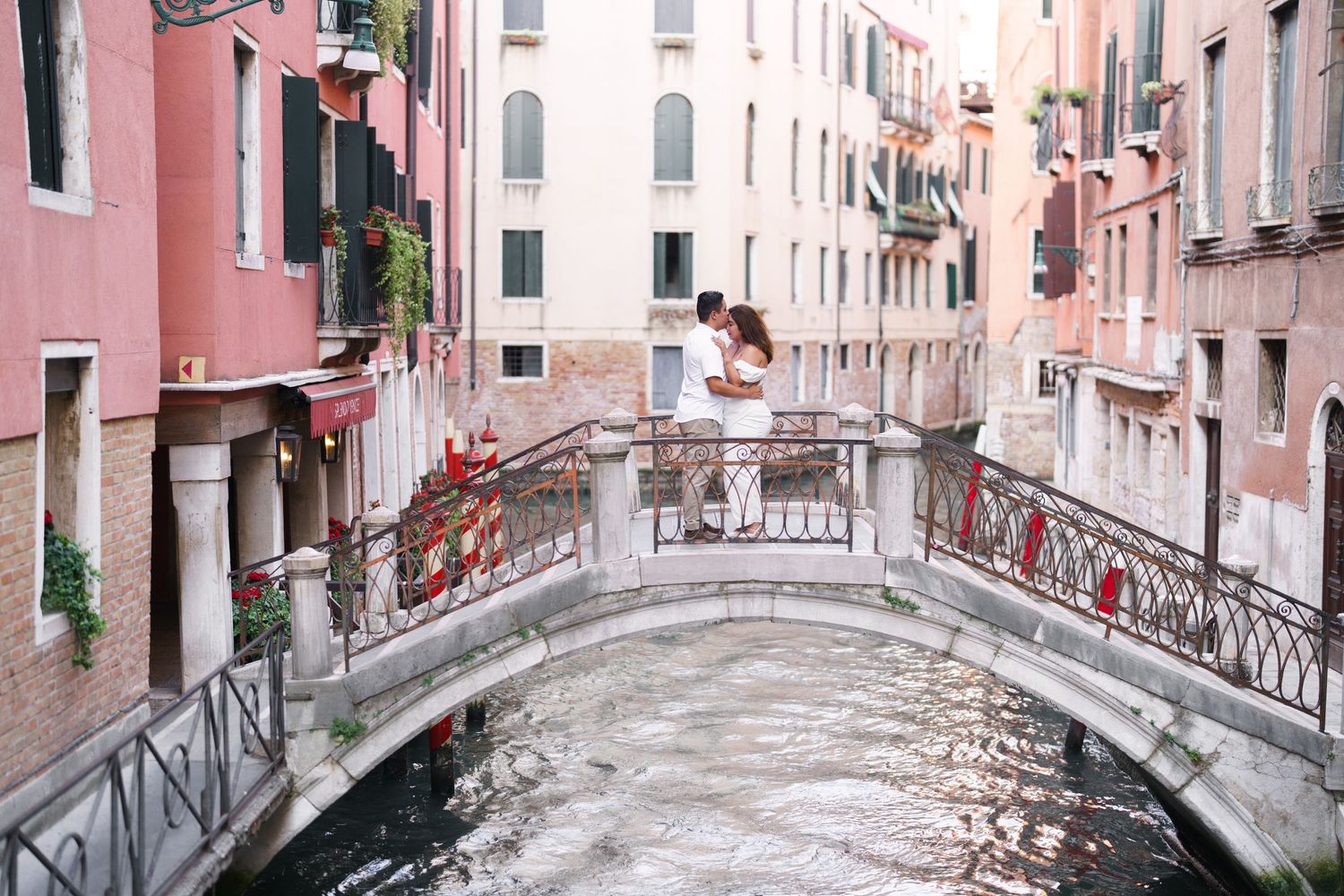 A scenic panoramic view of small bridges crossing Venetian canals with pink buildings and traditional architecture.