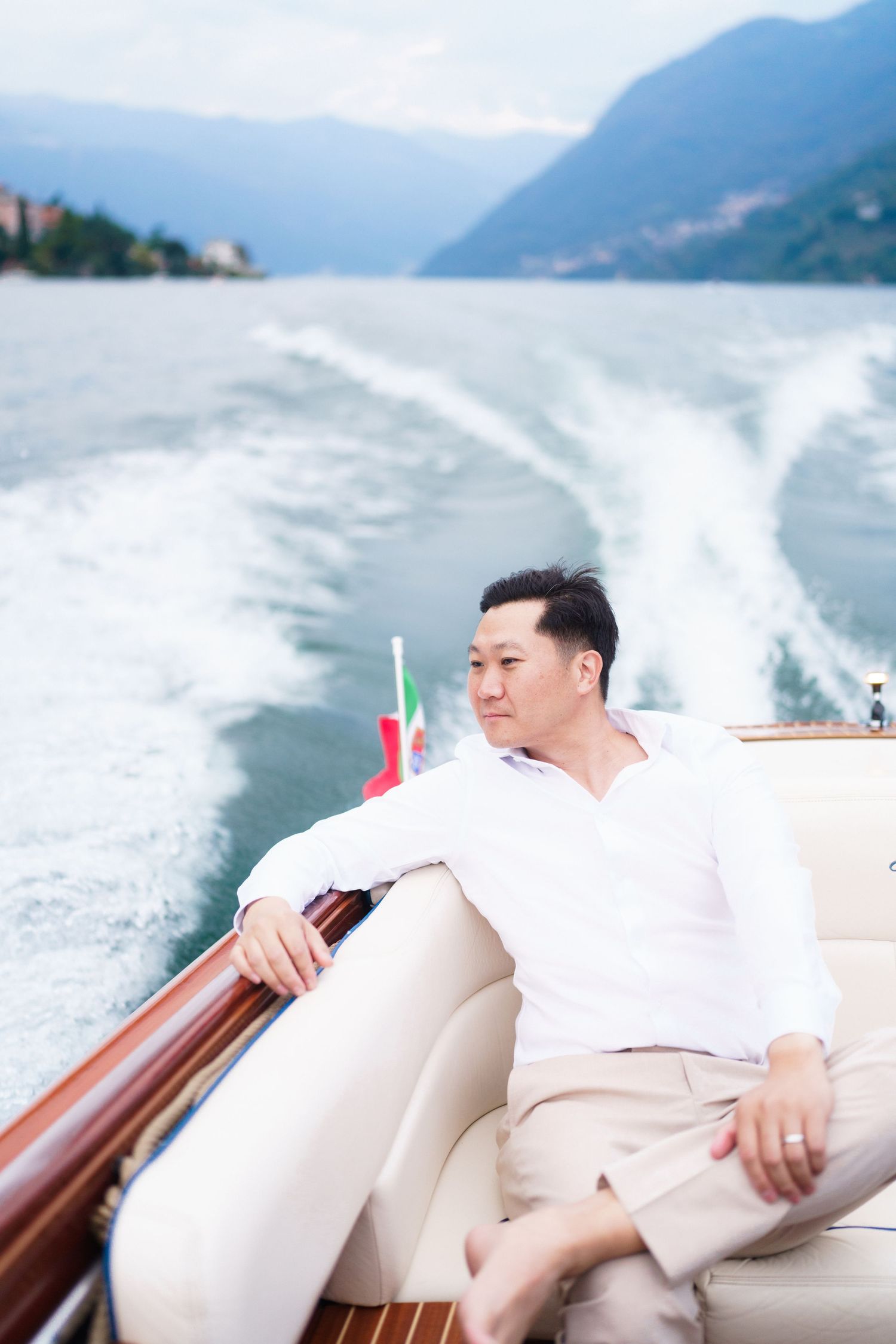 A person relaxes on a white leather seat of a luxury boat while cruising through scenic mountain waters.