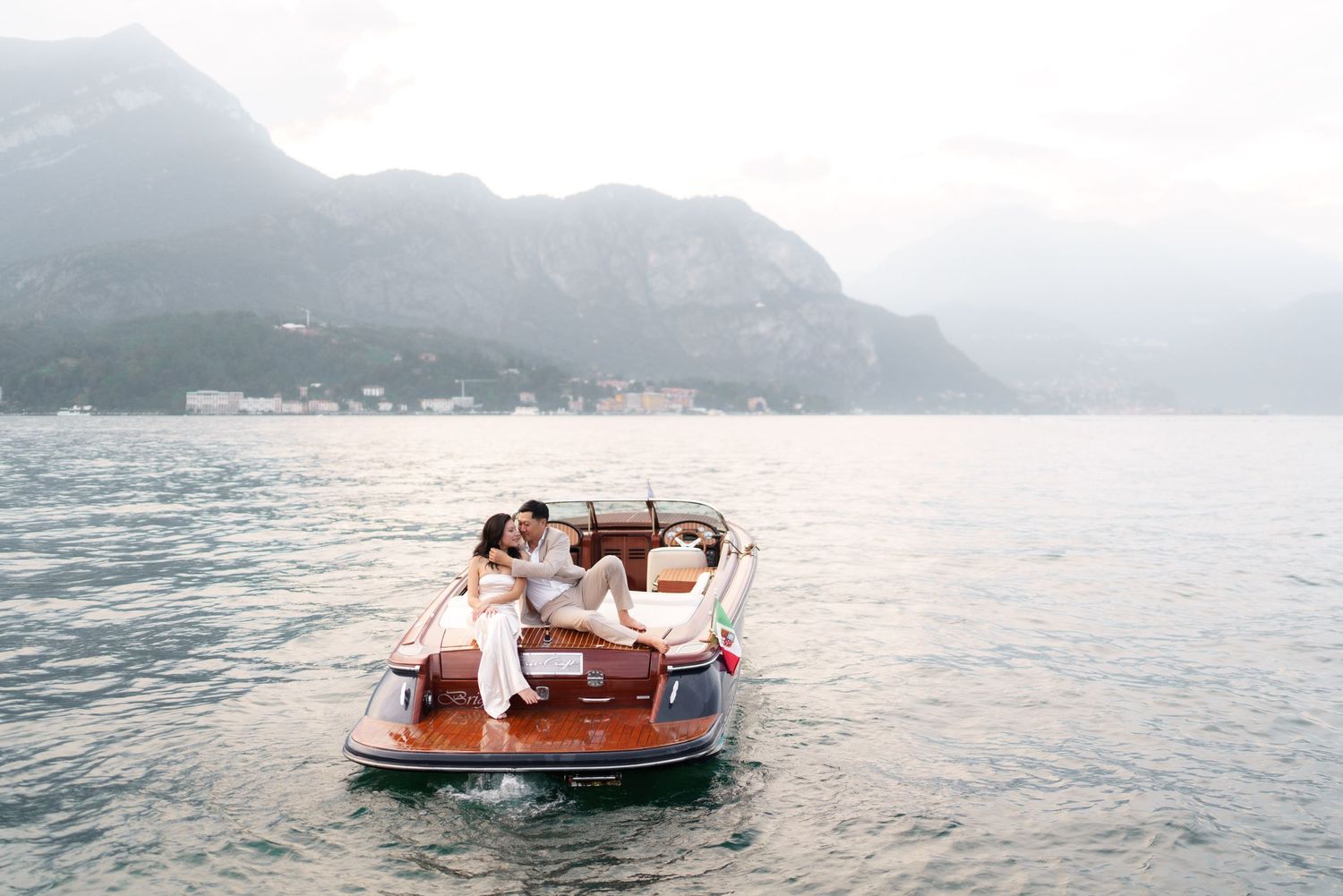 A wooden boat glides across Lake Como with mountains and misty scenery in the background.