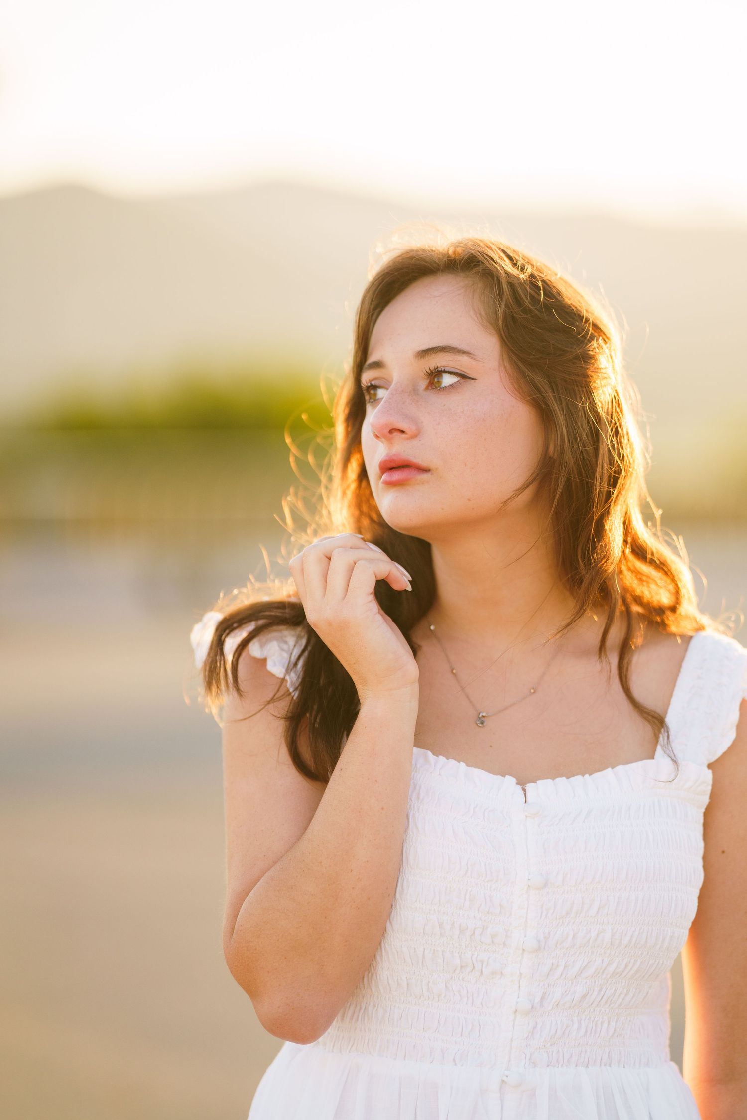 Woman in white dress poses in golden sunlight during sunset photoshoot outdoors.
