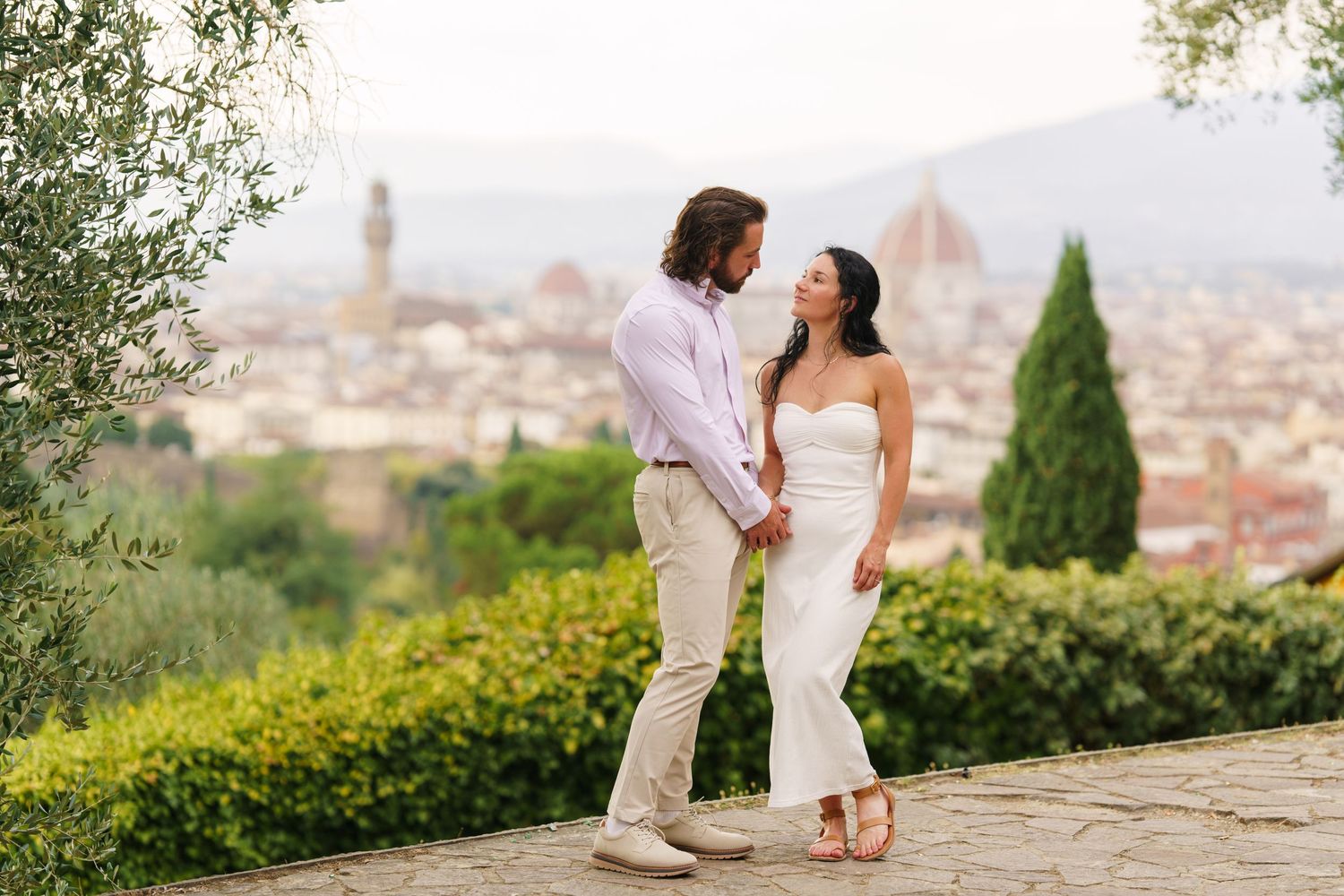 A couple shares a romantic moment overlooking Florence, Italy during sunset with the city skyline in the background.
