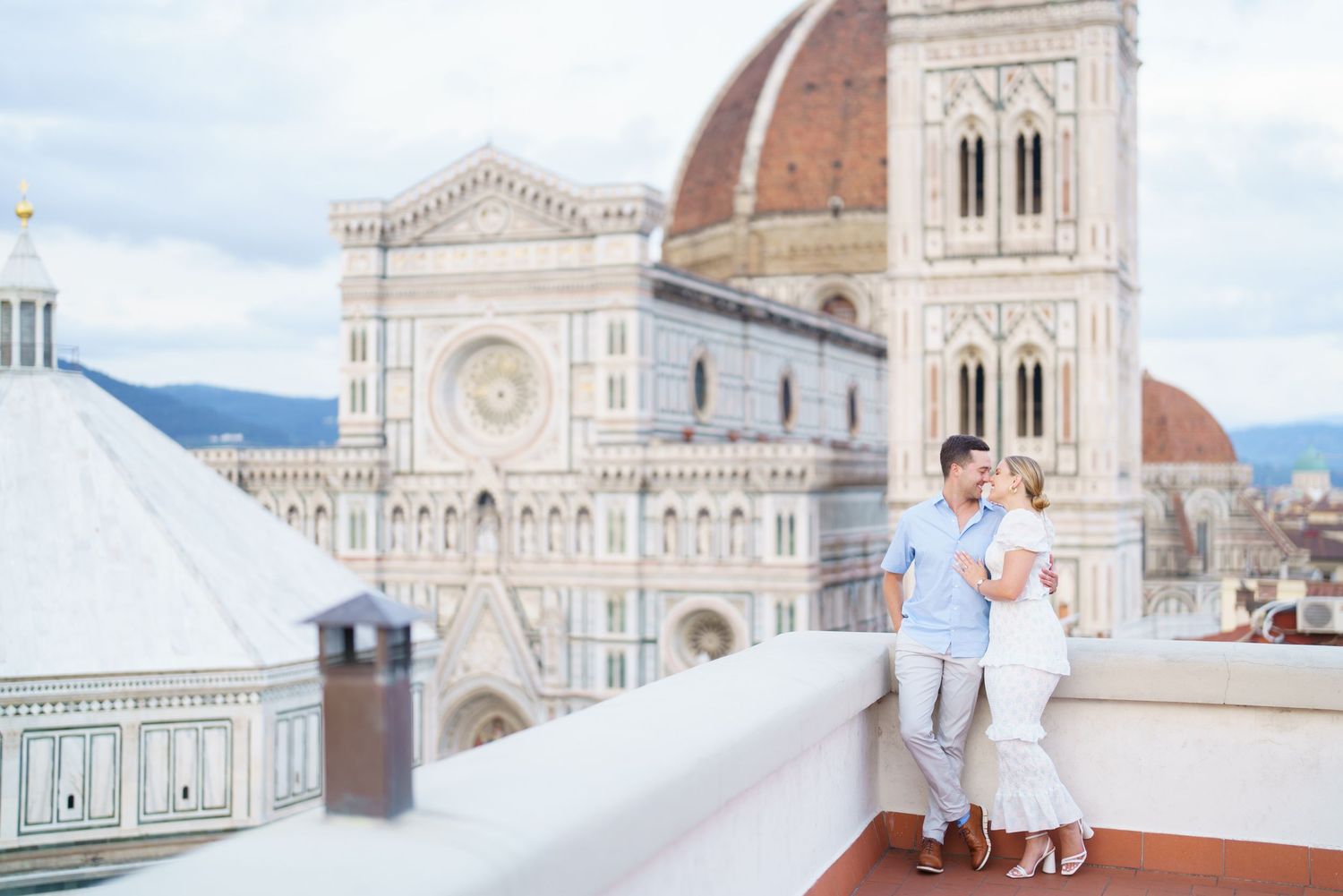 Two people in white outfits stand on the rooftop terrace overlooking the Florence Cathedral and cityscape in Italy.