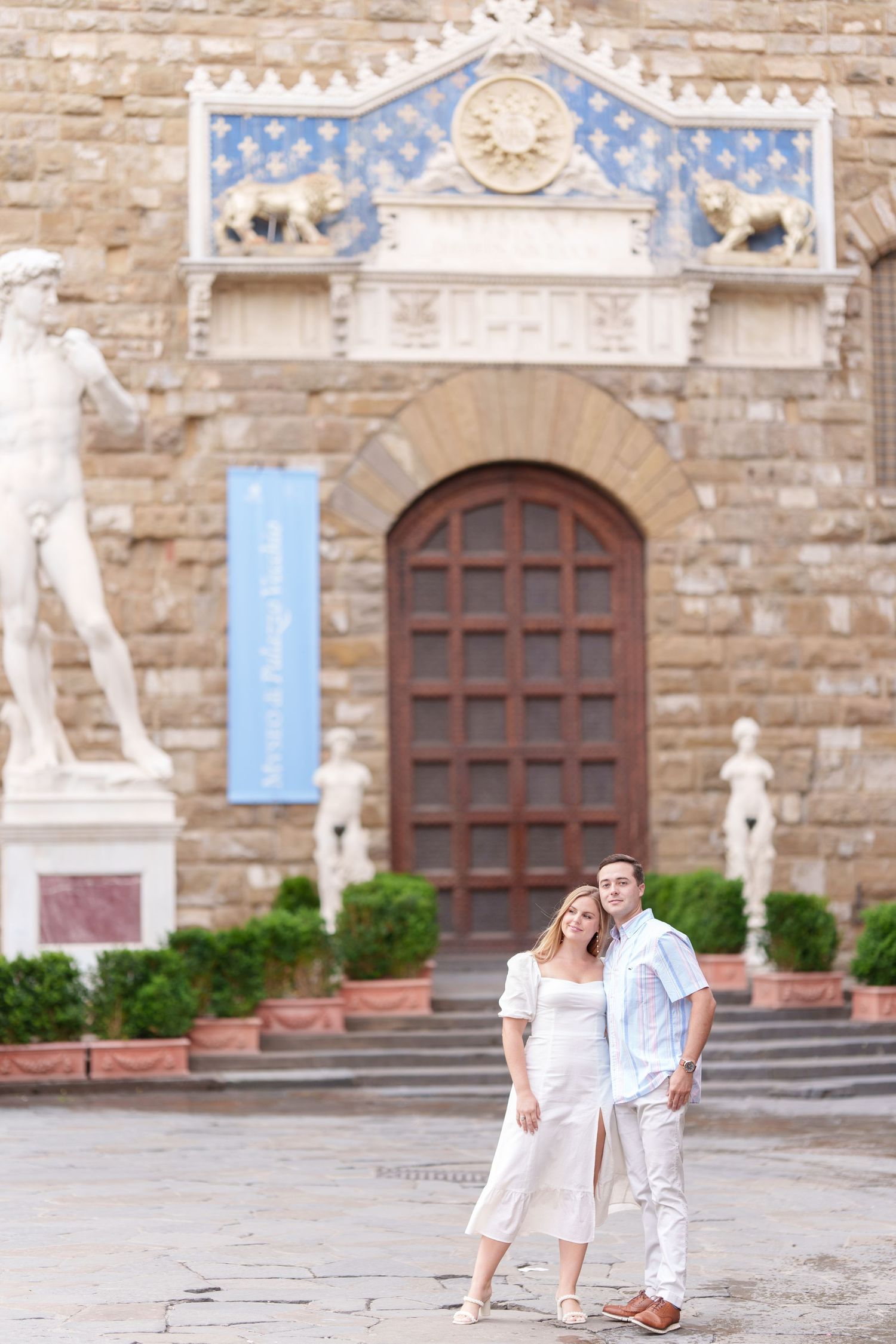 A couple stands in front of an ornate stone building entrance with classical statues and architectural details in Florence, Italy.