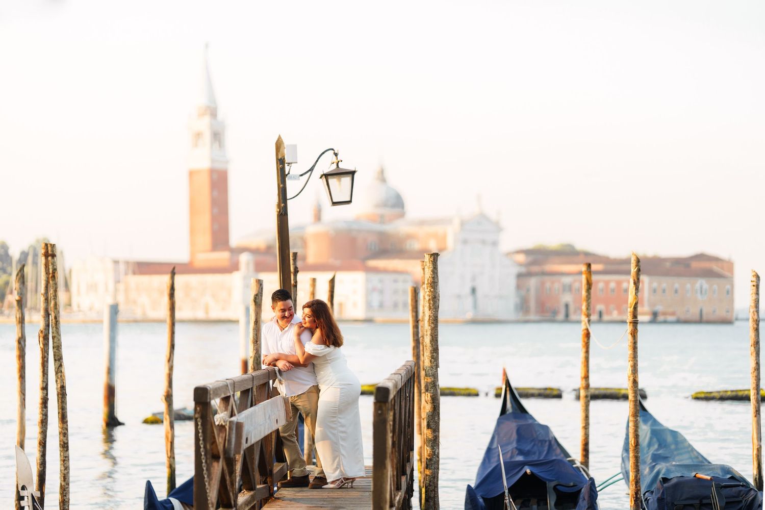 photographer venRomantic couple enjoying sunset view of Venice from wooden dock with gondolas and San Giorgio Maggiore church in background.