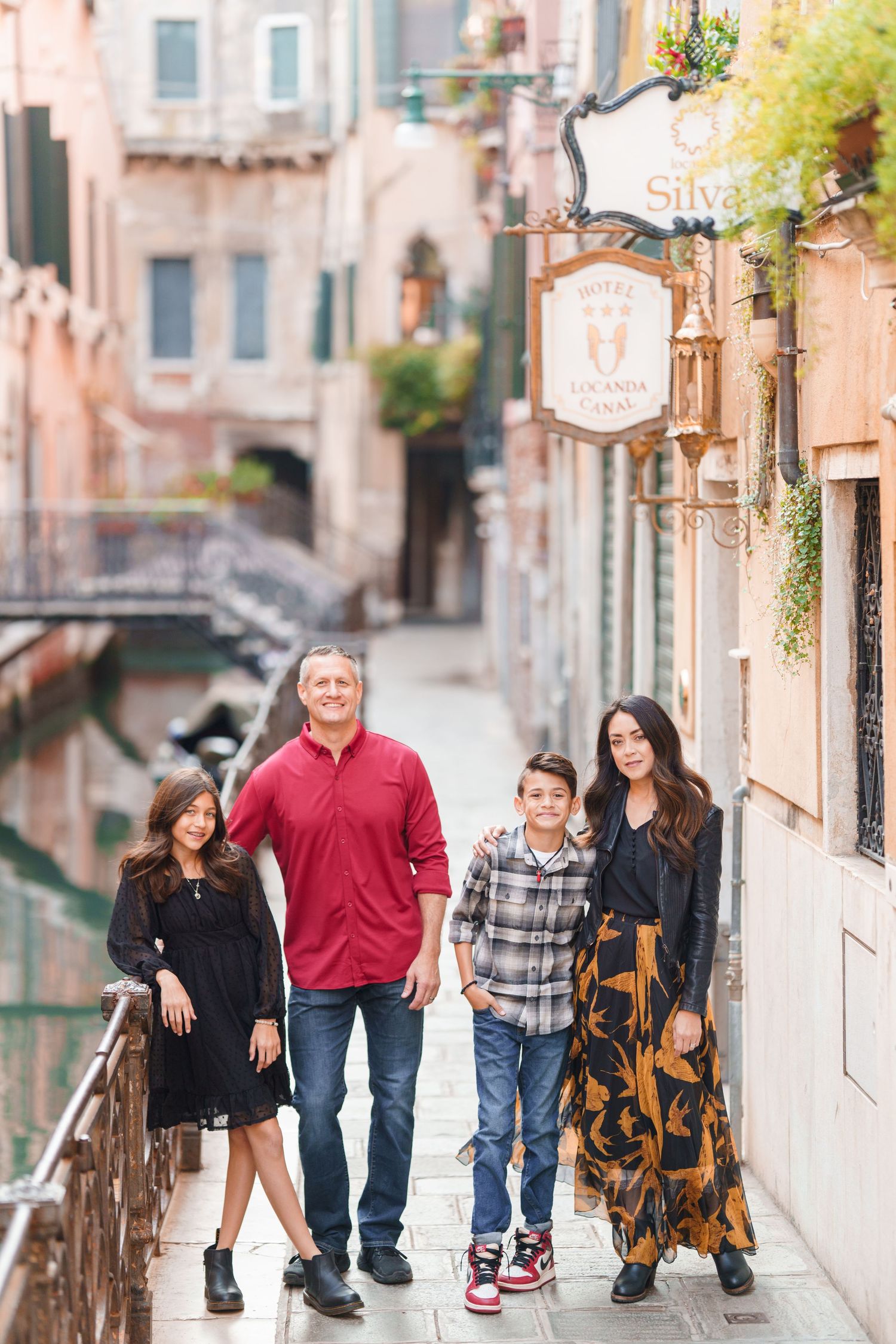 Family walking together along a charming narrow street in Venice with historic buildings and bridges in background.