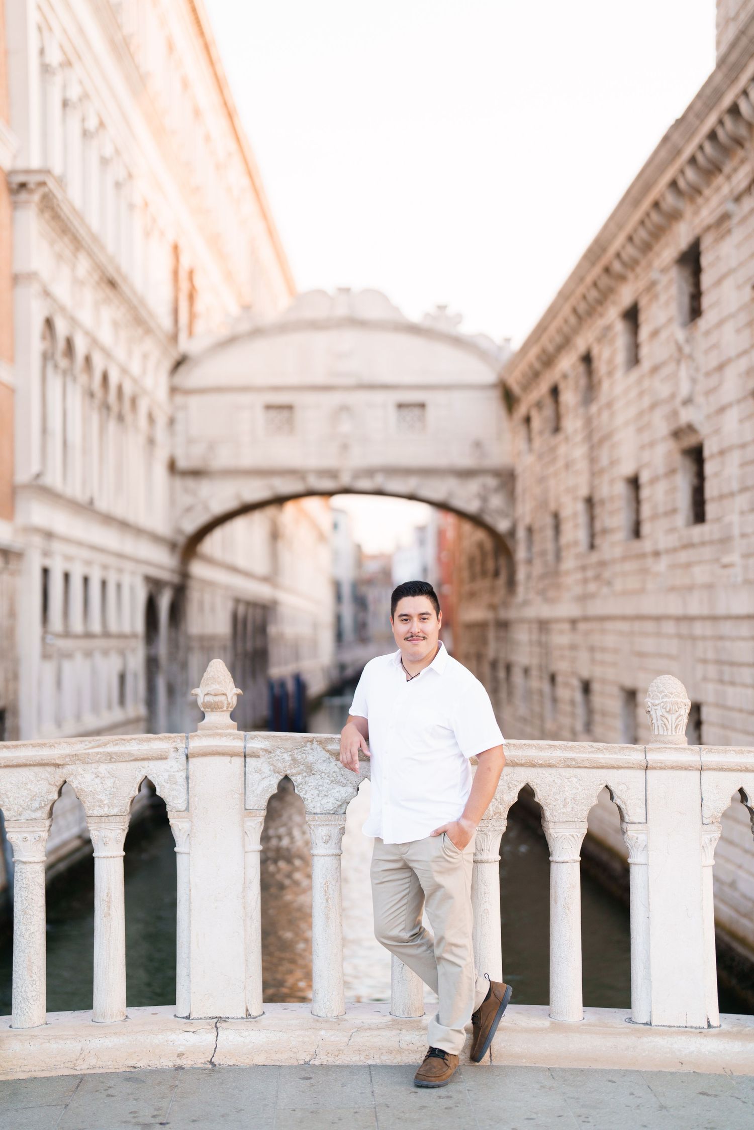 A person in white clothing sits on an ornate stone balustrade in a classical European architectural setting.