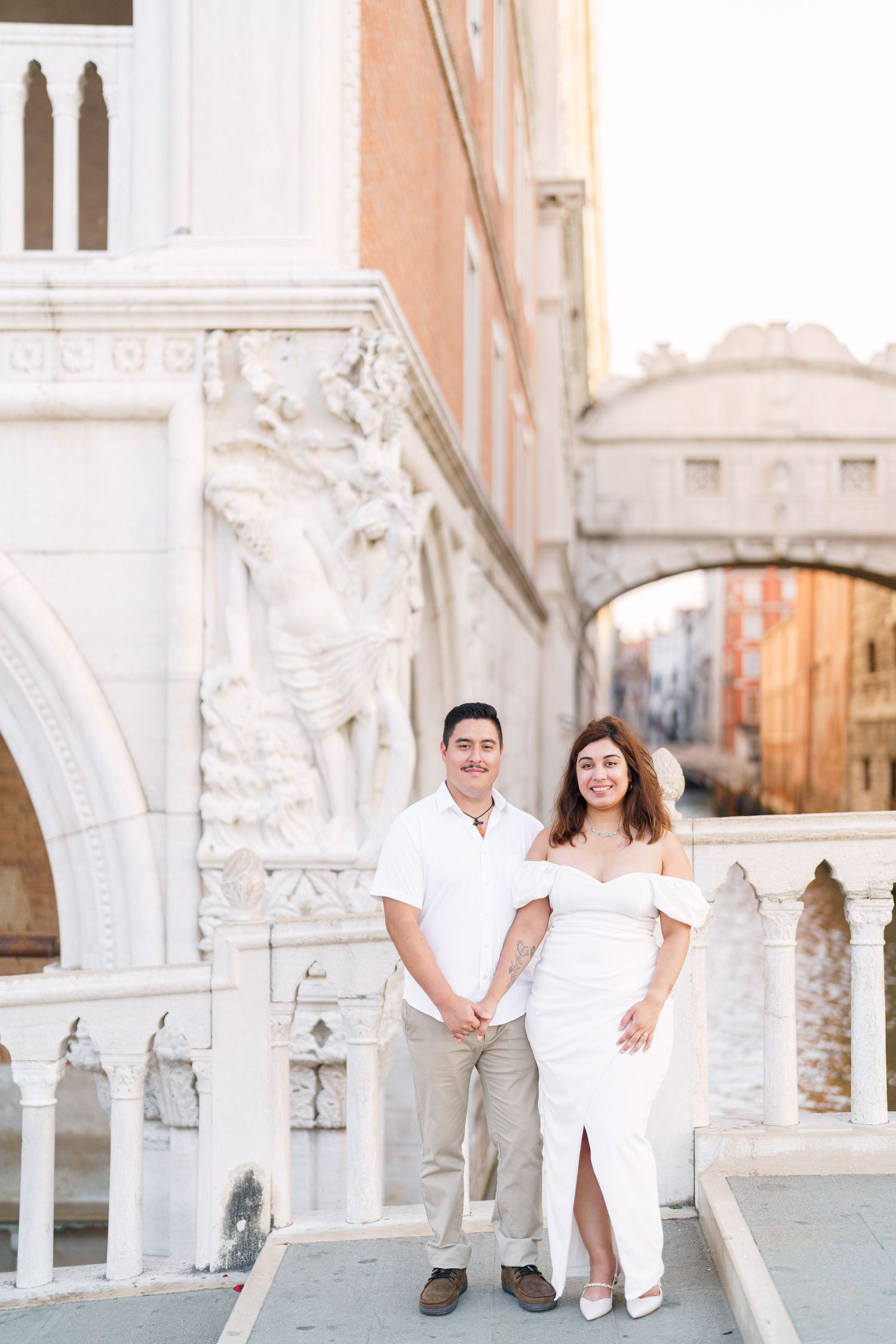 A romantic couple photoshoot at St. Mark's Square in Venice with white marble columns and arches in the background.