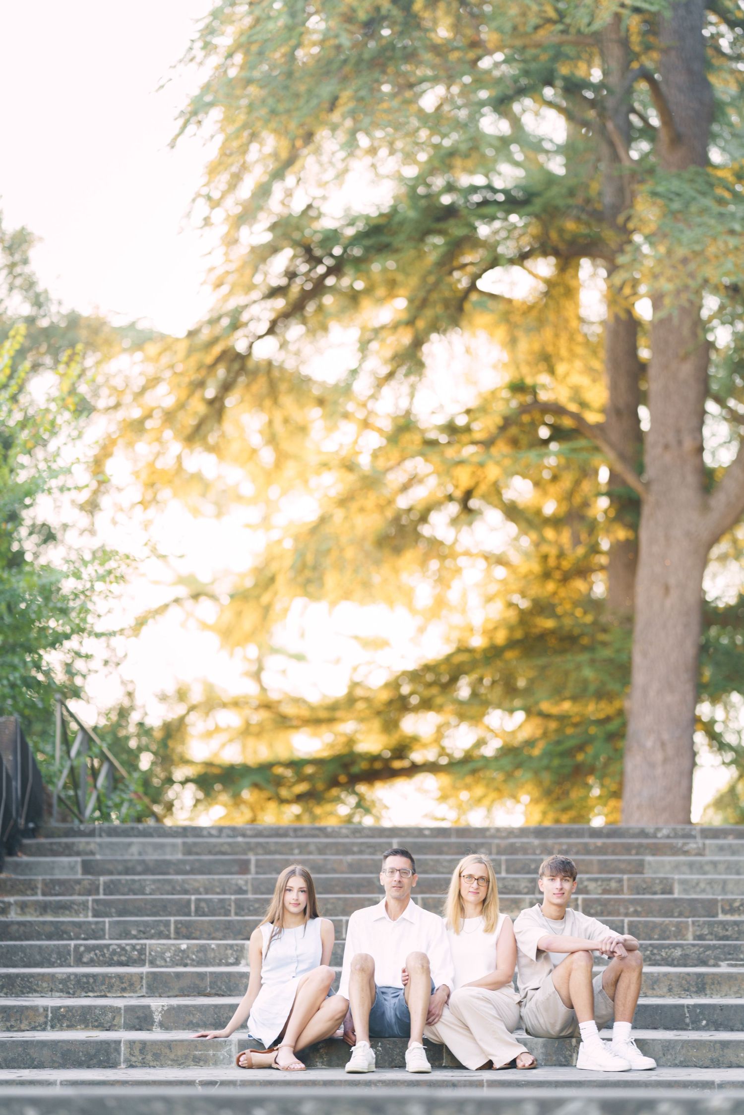 Four people relax on stone steps under tall evergreen trees during a warm golden sunset.