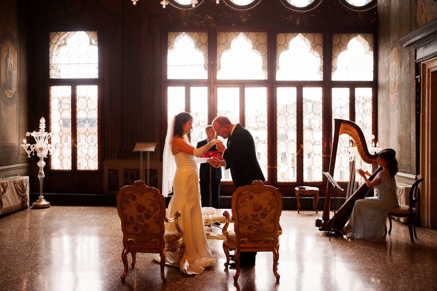 A harpist performs in an elegant room with large windows and ornate architectural details.