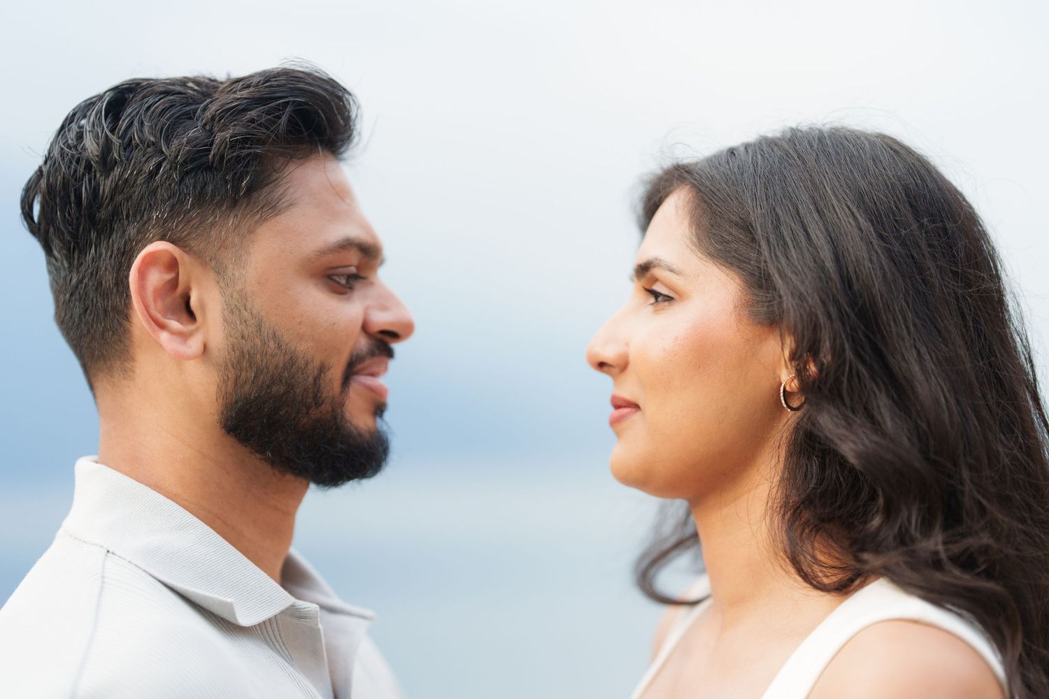 Two people in white outfits stand close together against a bright background during a romantic photoshoot.