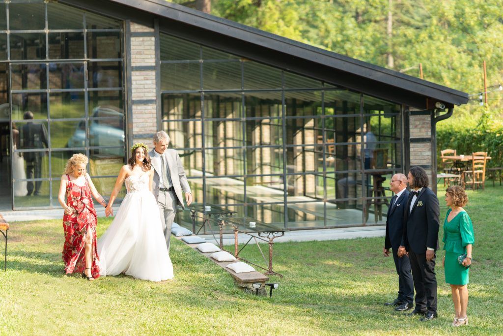 Elegant outdoor wedding ceremony setup with guests mingling near a modern glass building.