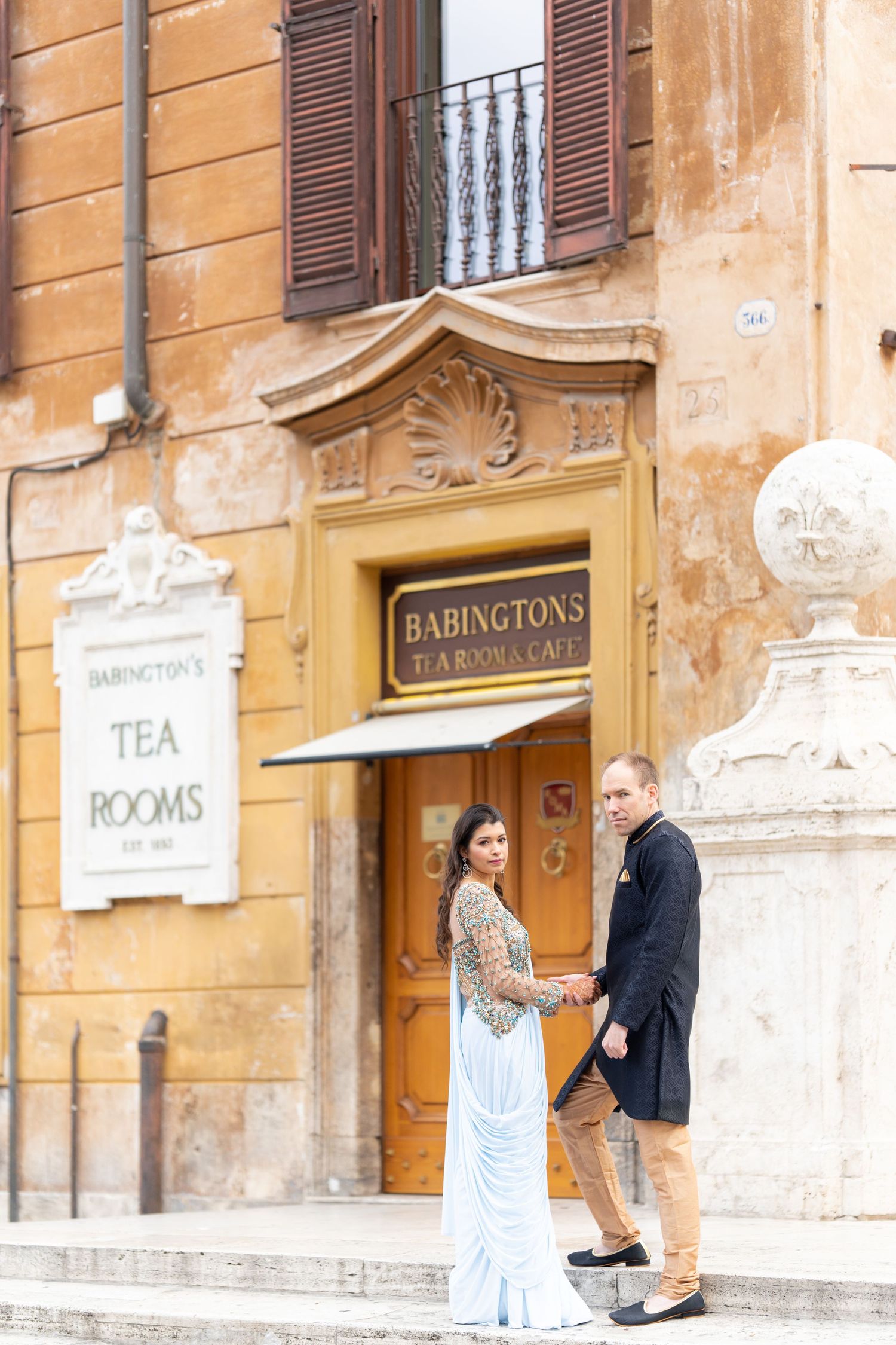 Couple posing in front of a historic building with weathered walls and wooden shutters.