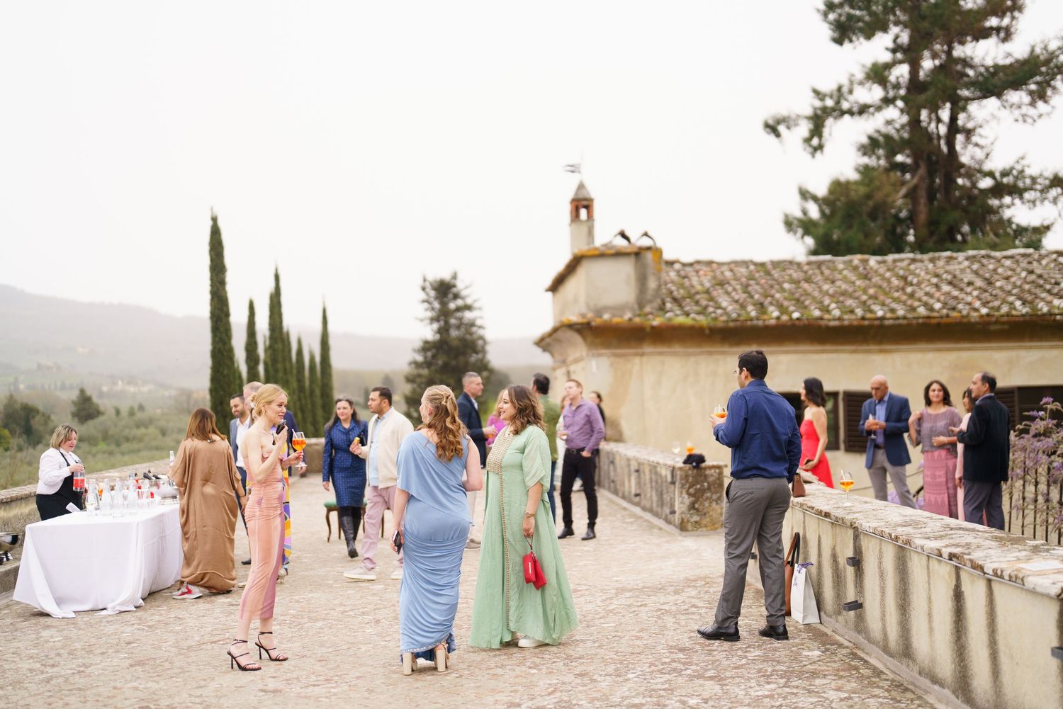 Wedding guests in colorful attire gathered on stone terrace with mountain views.