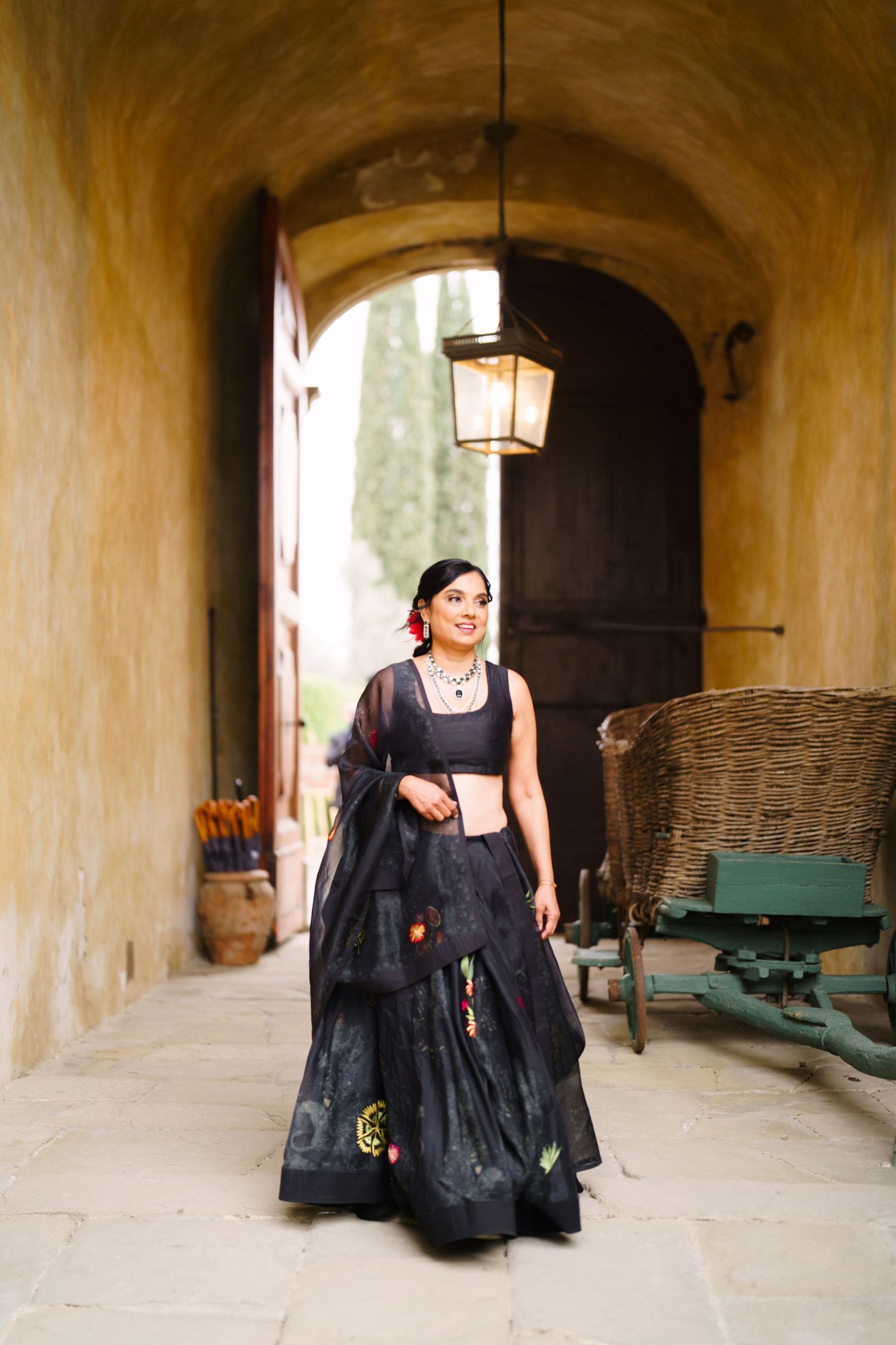 Person in a black dress seated in an arched stone hallway with rustic decor.