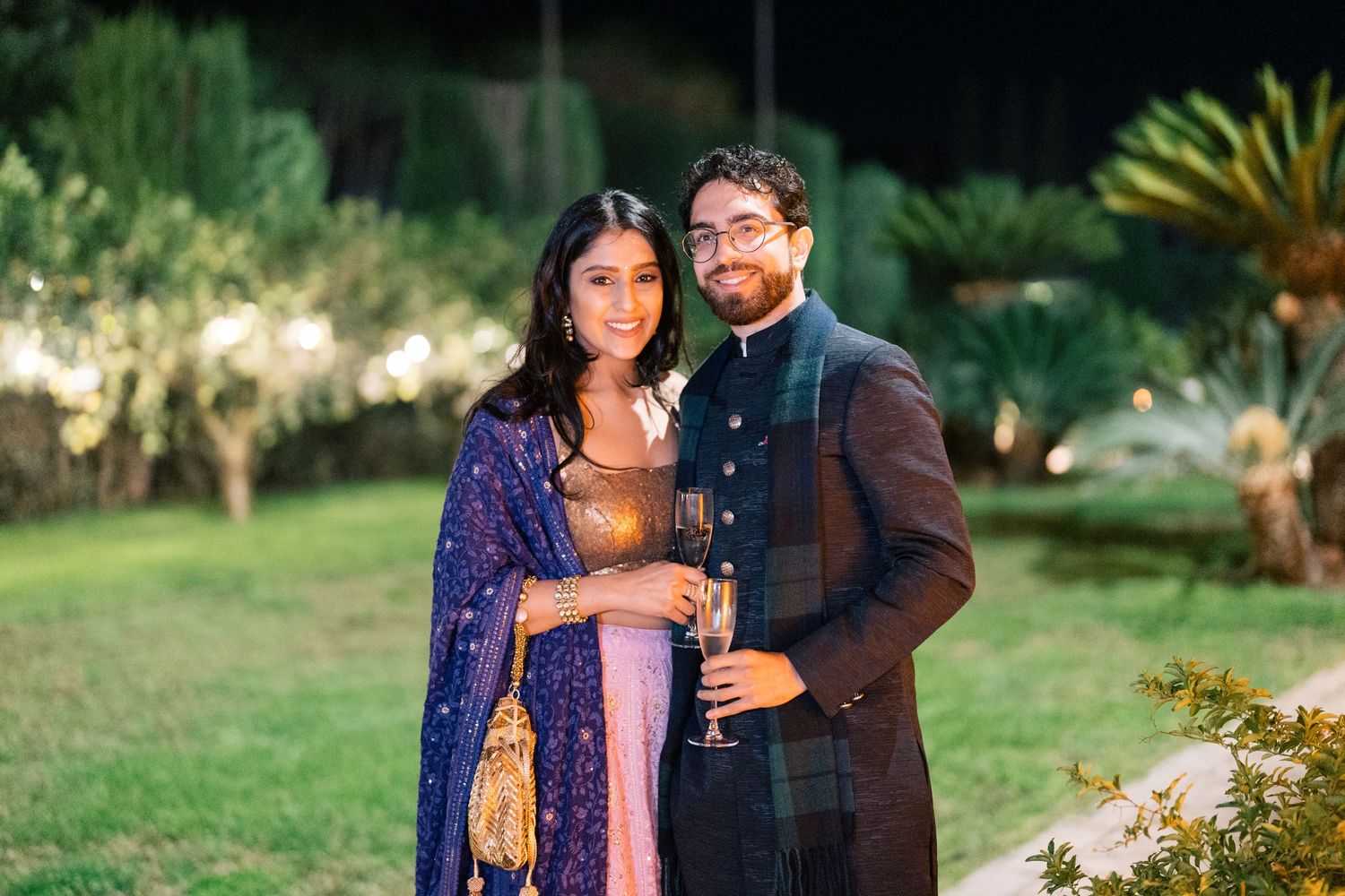 Couple in traditional Indian attire poses in garden setting during evening photoshoot.