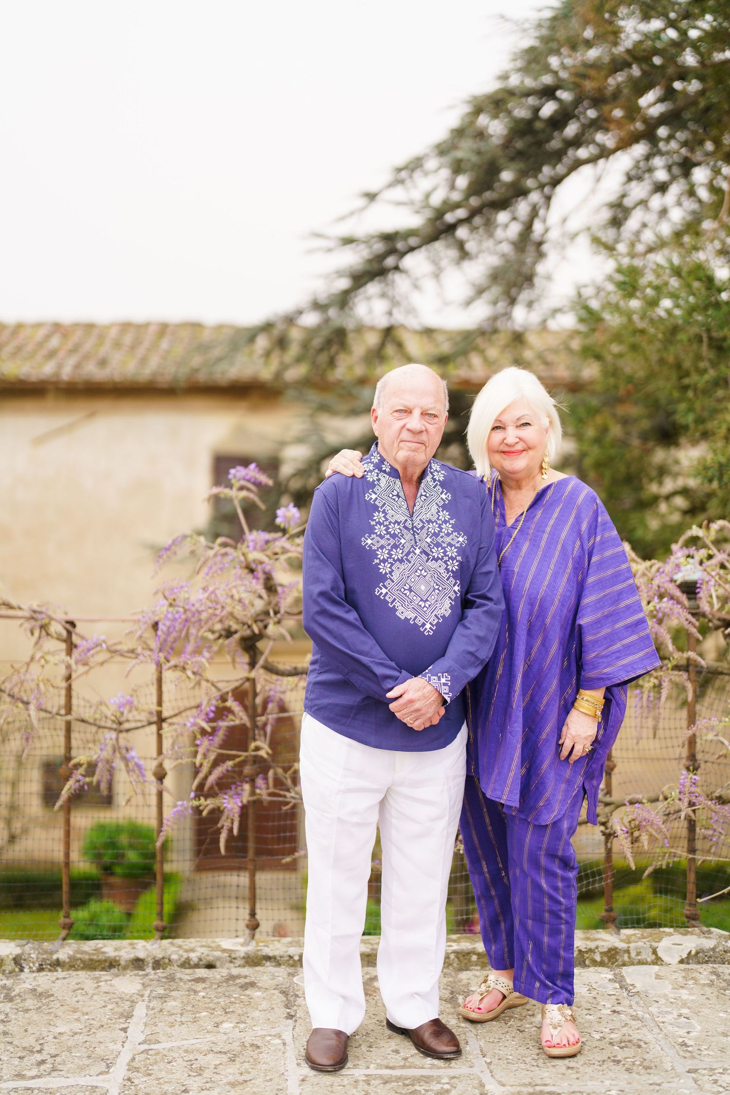 Couple in coordinating purple outfits standing together by flowering trees.