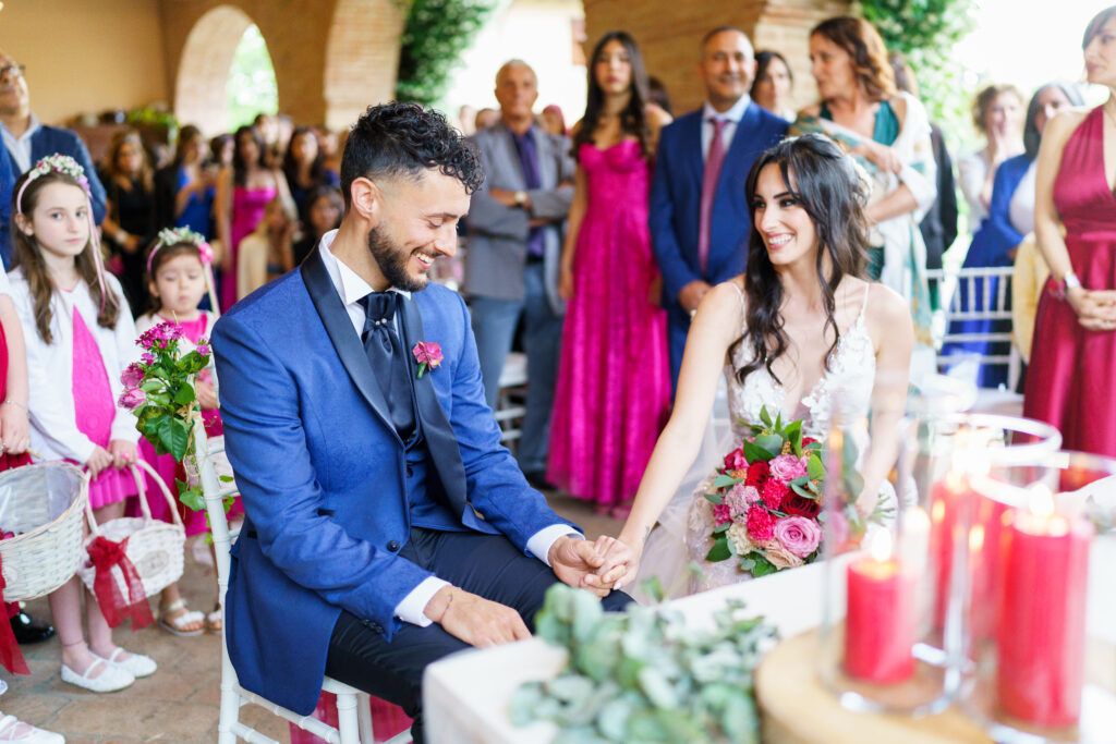 Couple participates in wedding ceremony under arched walkway with pink floral arrangements.