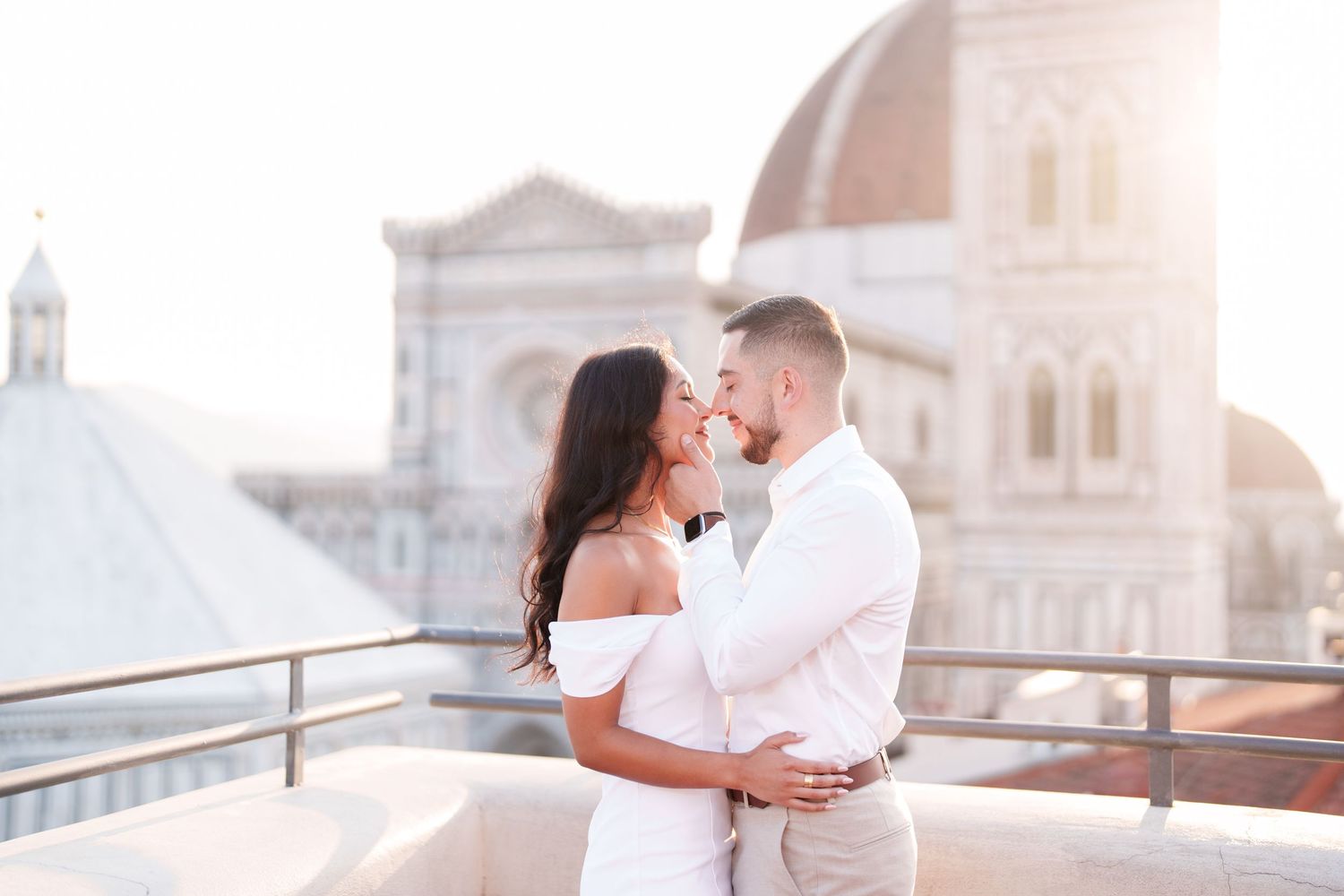 A romantic couple shares a tender kiss during their rooftop wedding ceremony at sunset in a European city.