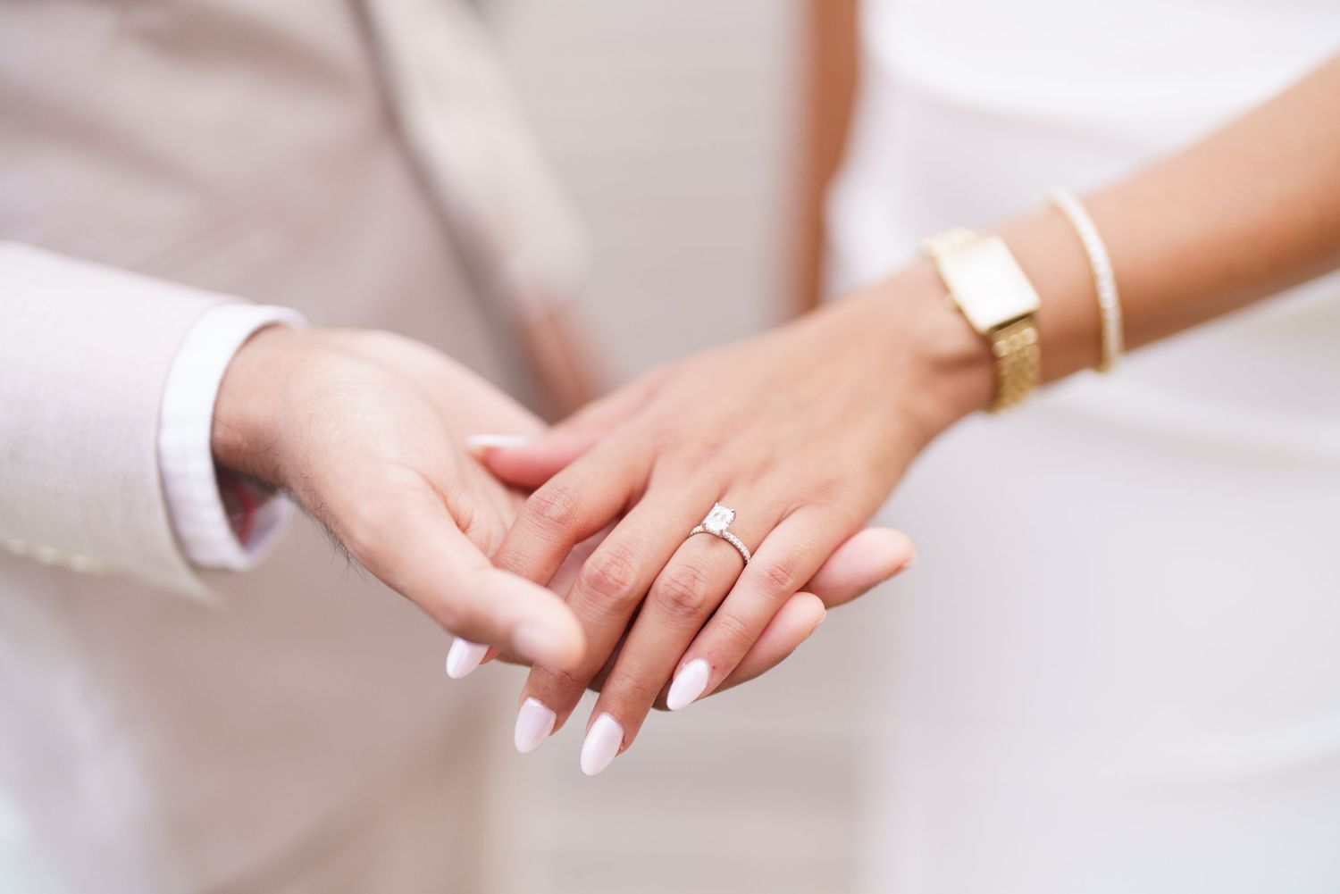 Two hands wearing wedding rings and bracelets touch gently in an intimate moment.