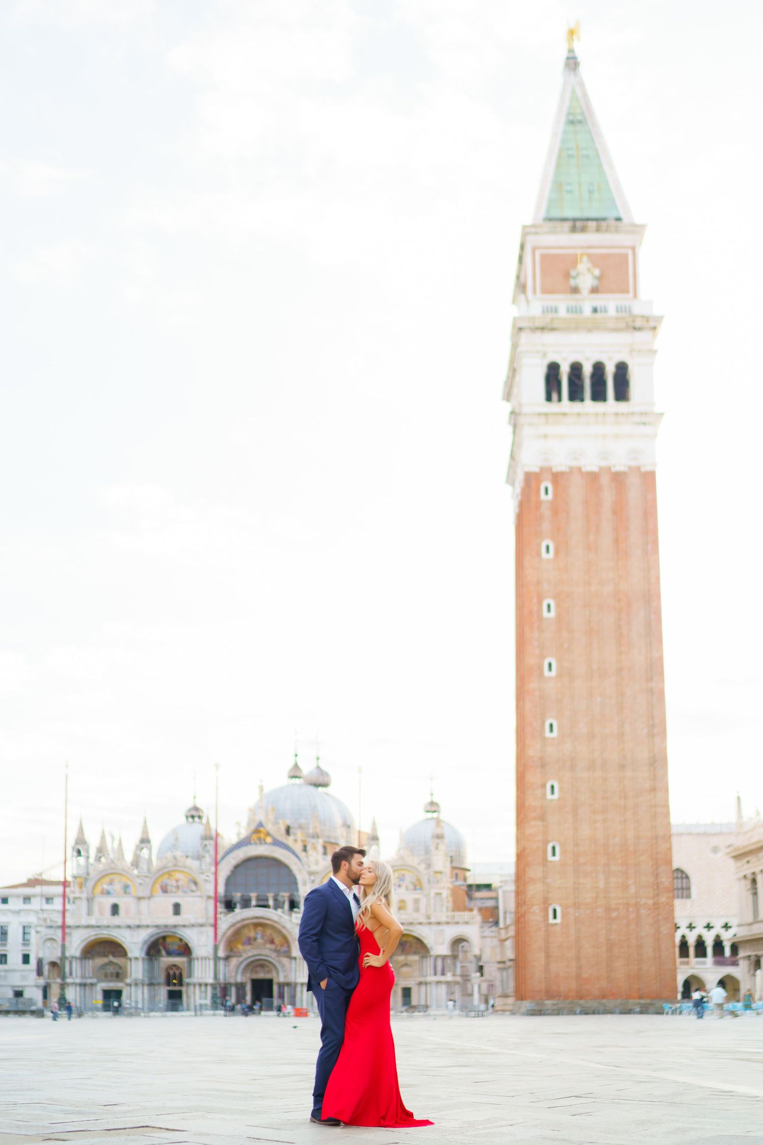 Romantic couple in formal attire poses in St Mark's Square in Venice with the iconic bell tower and basilica in background.