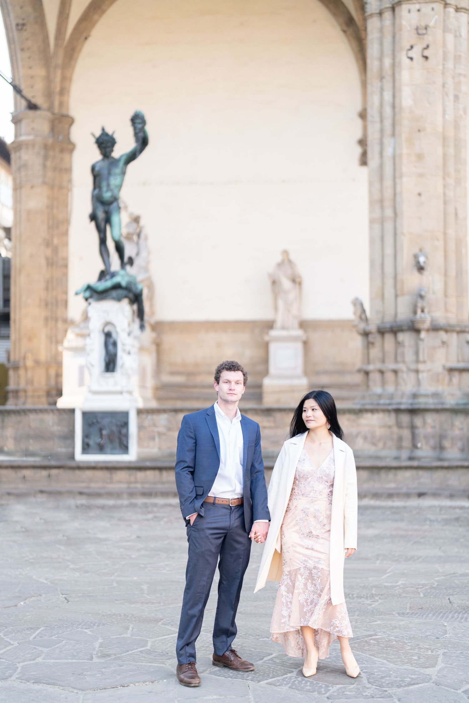 A couple stands together at the Loggia dei Lanzi in Florence, Italy with historic statues in the background.