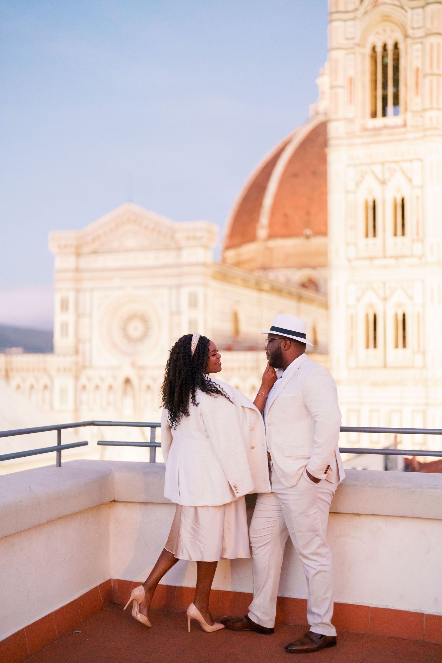 Elegant Black couple in white attire sharing a romantic moment on a rooftop with Florence Cathedral dome backdrop.
