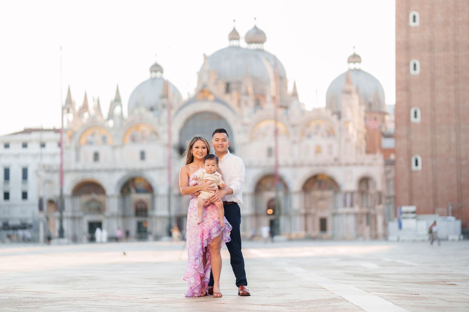 Family posing in St. Mark's Square, Venice, with the iconic Basilica di San Marco in the background at golden hour.