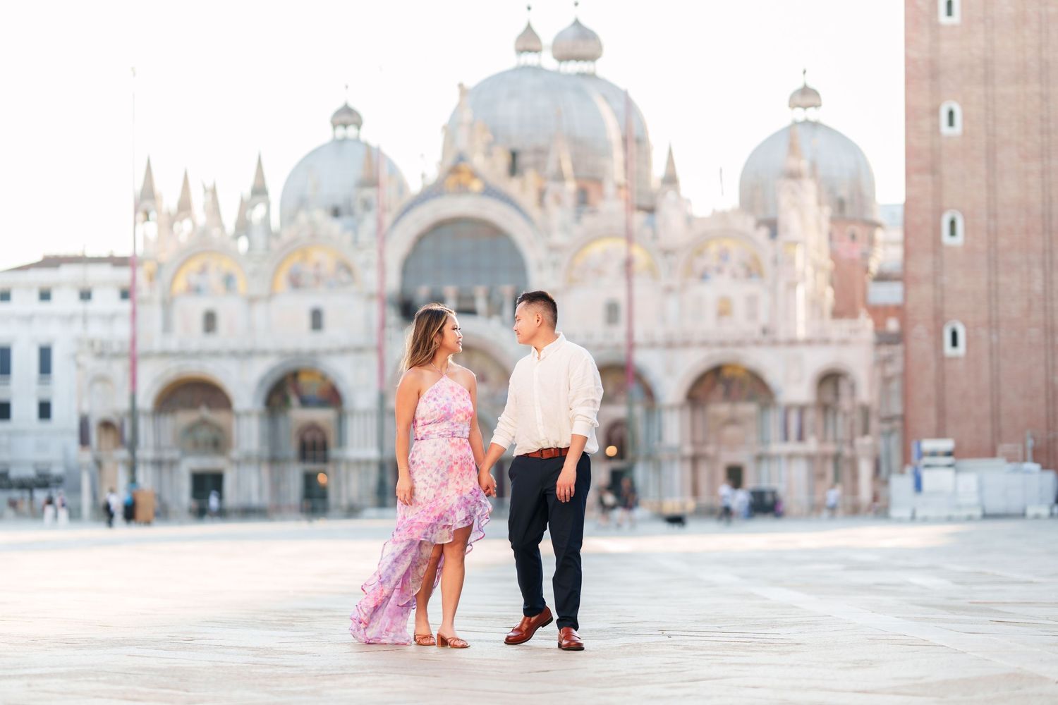 Couple holding hands in Piazza San Marco with St. Mark's Basilica backdrop in Venice, Italy.