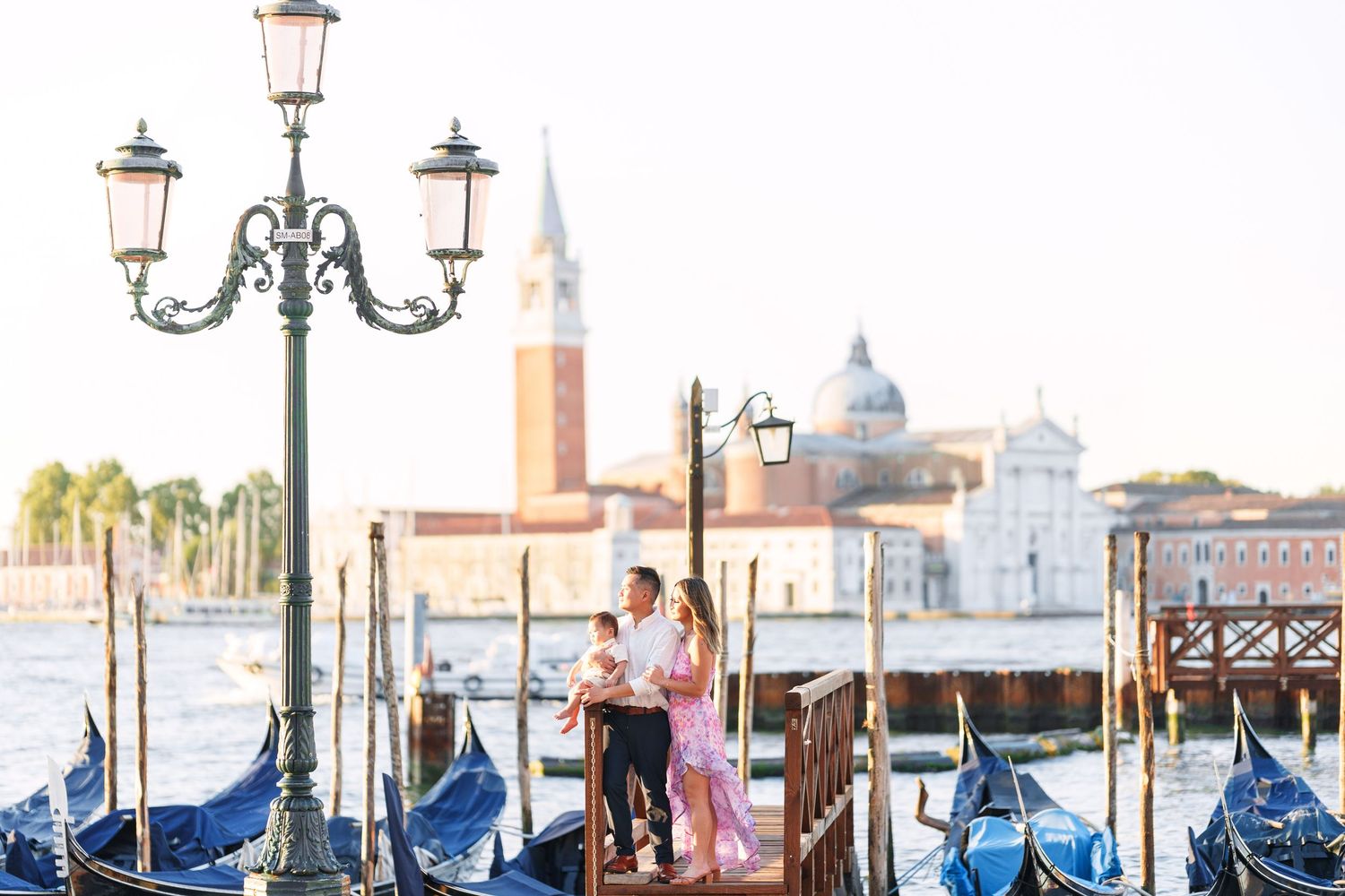 Couple embracing on a gondola dock in Venice, Italy, with gondolas and San Giorgio Maggiore church in the background.