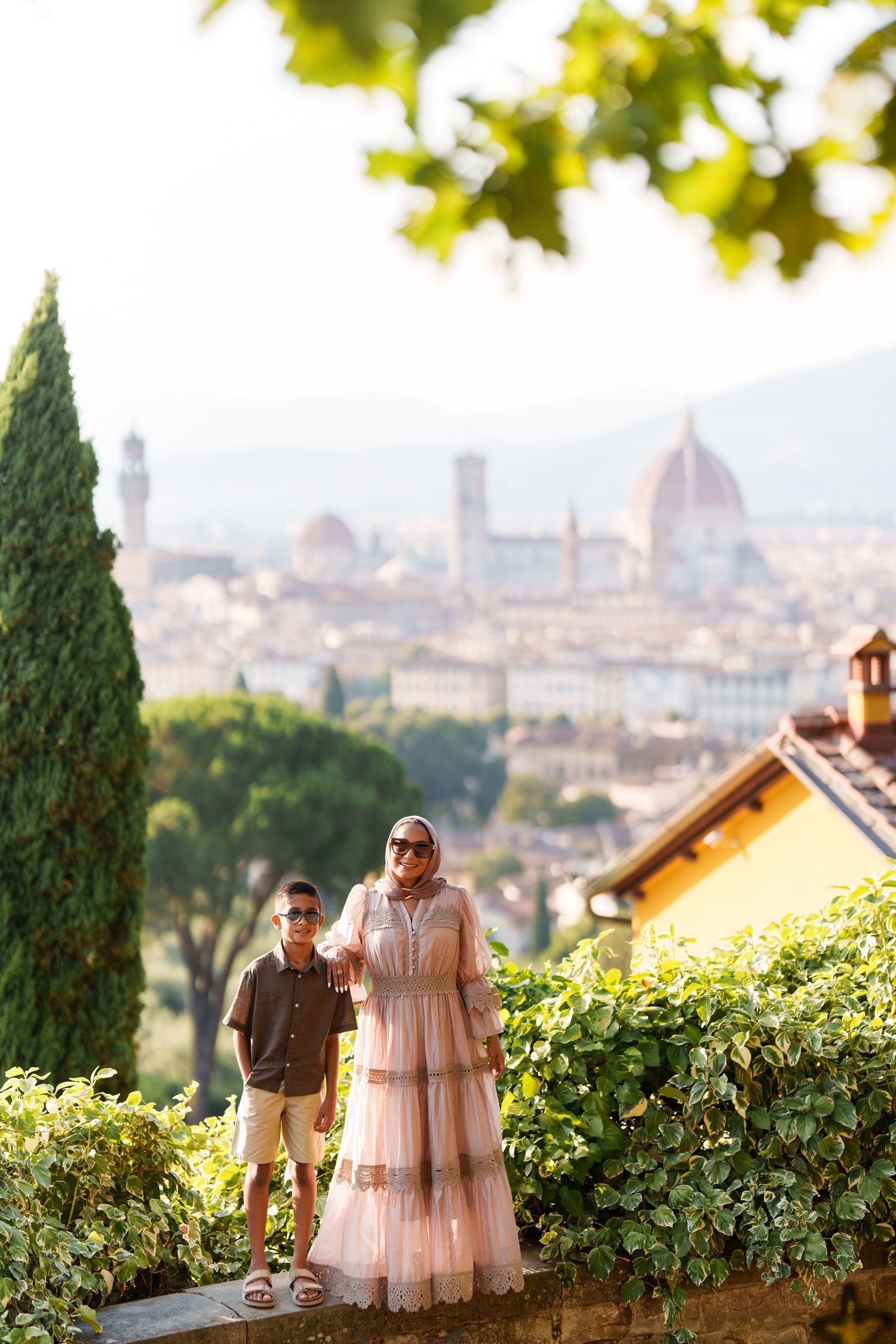 Woman in pink dress and boy pose with Florence skyline and Duomo cathedral in background on sunny day.