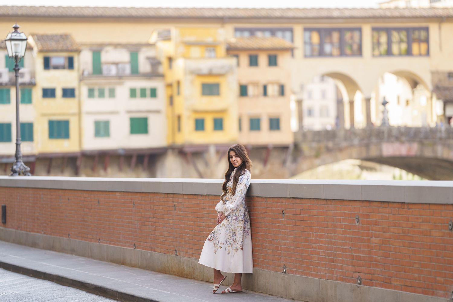 Woman in floral dress posing on bridge near Ponte Vecchio, Florence, Italy on sunny day.