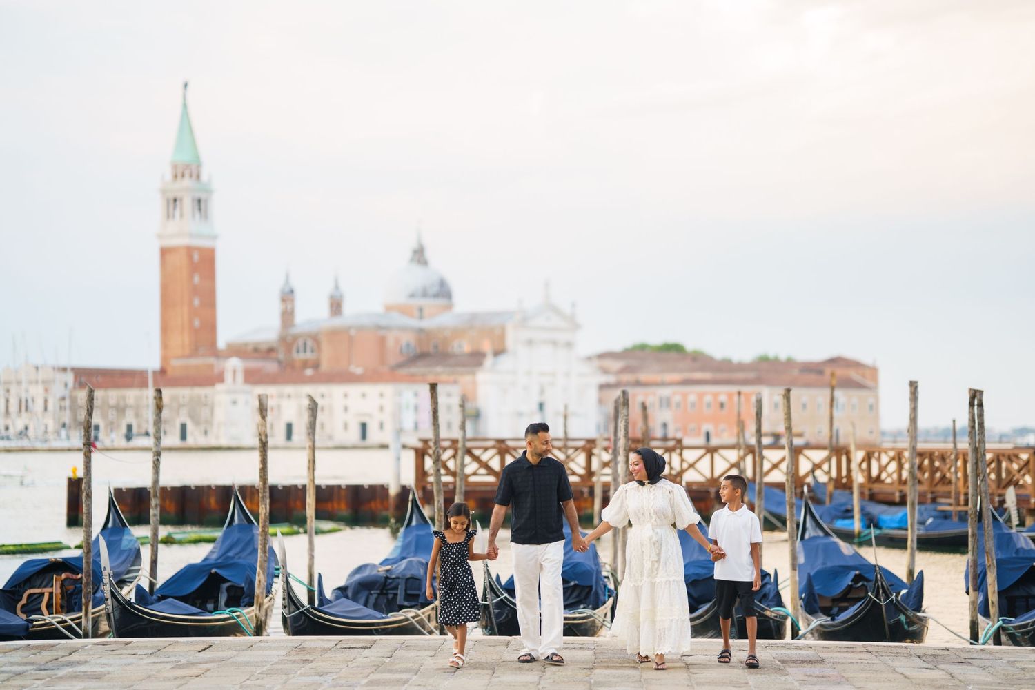 Family of four posing by gondolas in Venice with San Giorgio Maggiore island visible in the background.