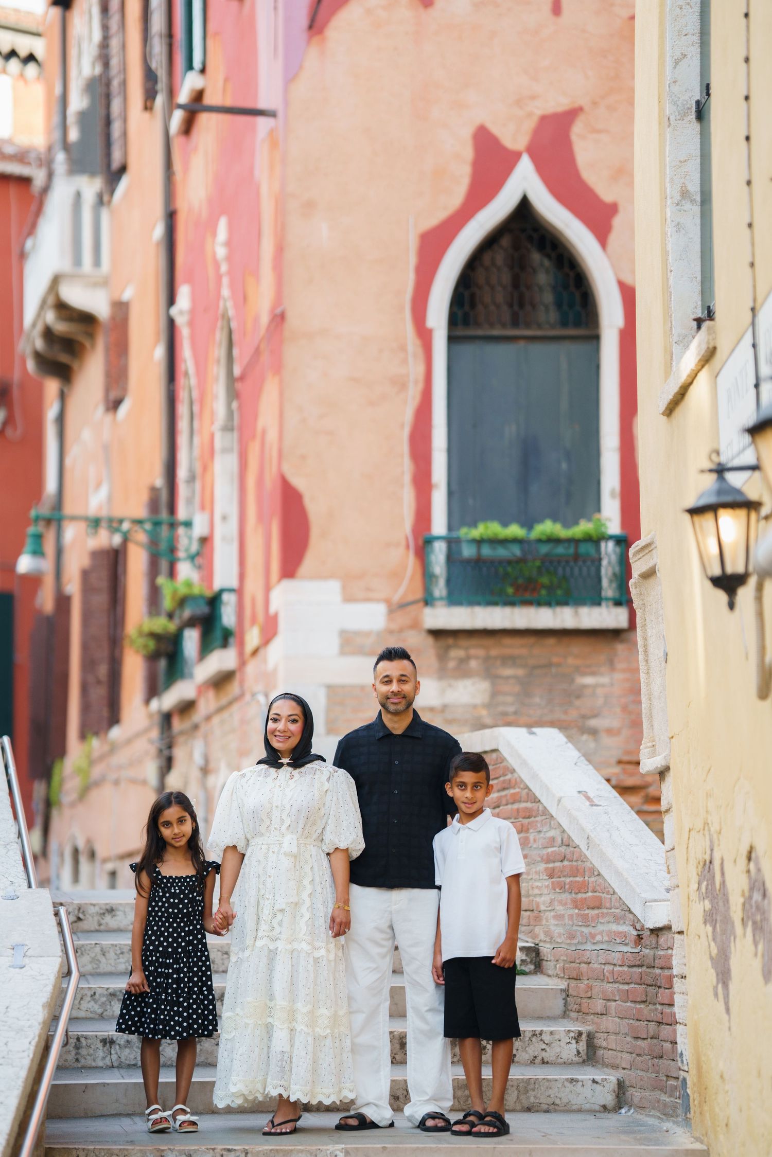 Family of four posing on steps in Venice, Italy, with colorful historic buildings in the background.