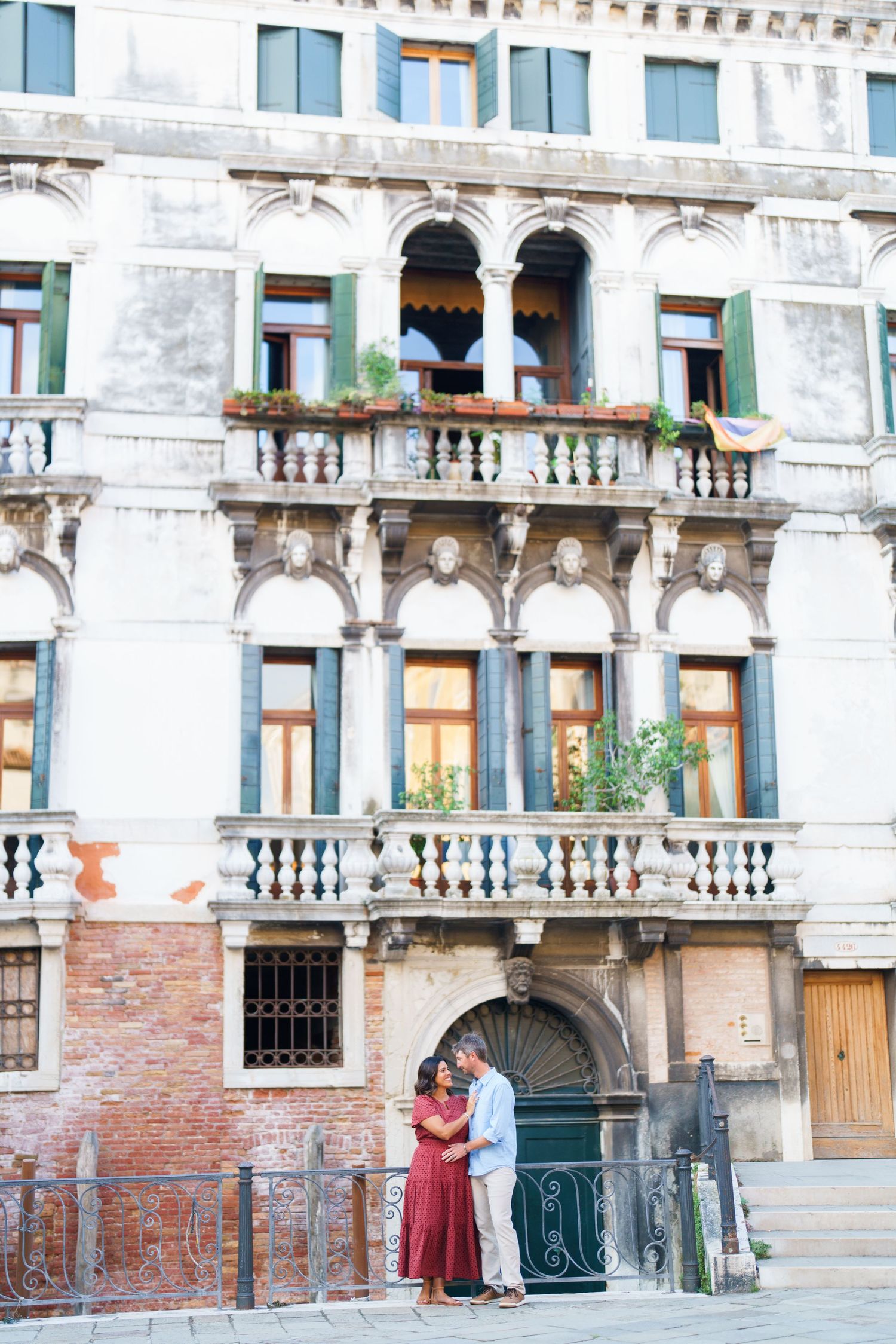 Couple embracing in front of ornate Venetian Gothic palazzo with arched windows and balconies in Venice, Italy.