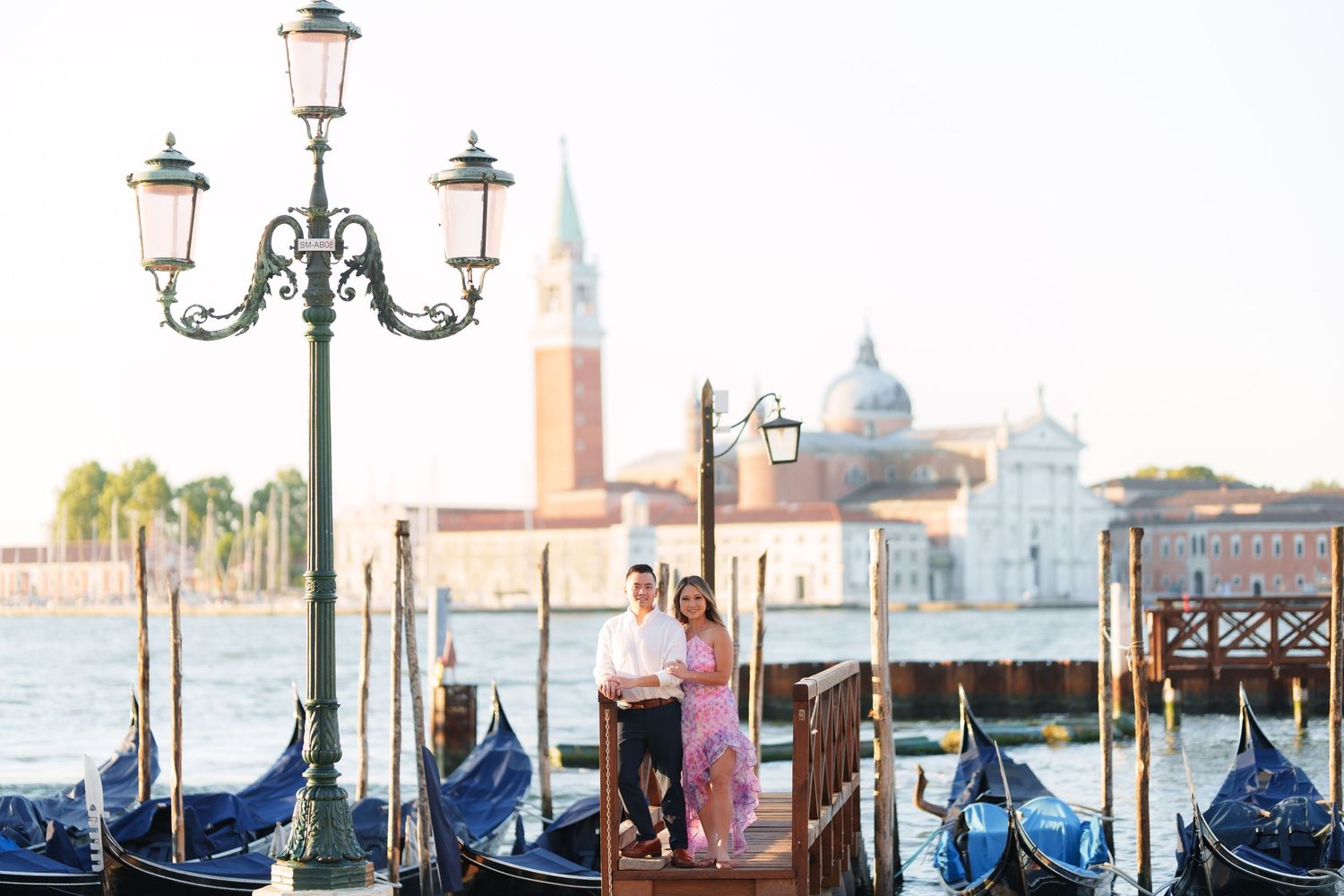 Couple standing on a dock in Venice Italy with gondolas and San Giorgio Maggiore church in background.