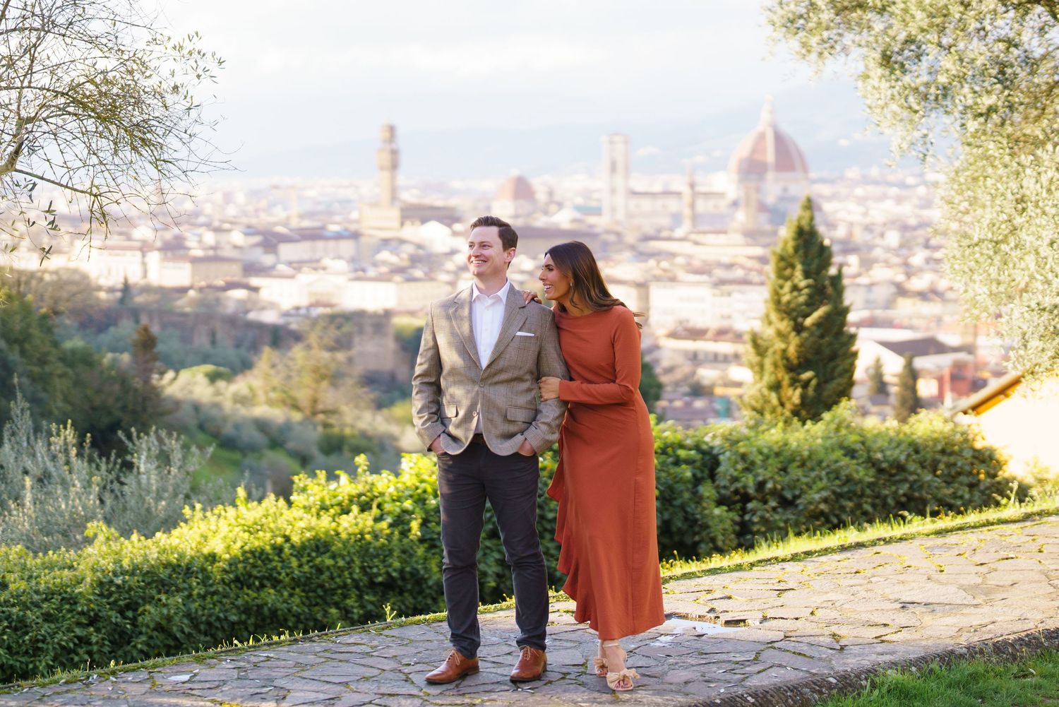 Couple smiling at each other with Florence skyline and Duomo cathedral in background on sunny day.