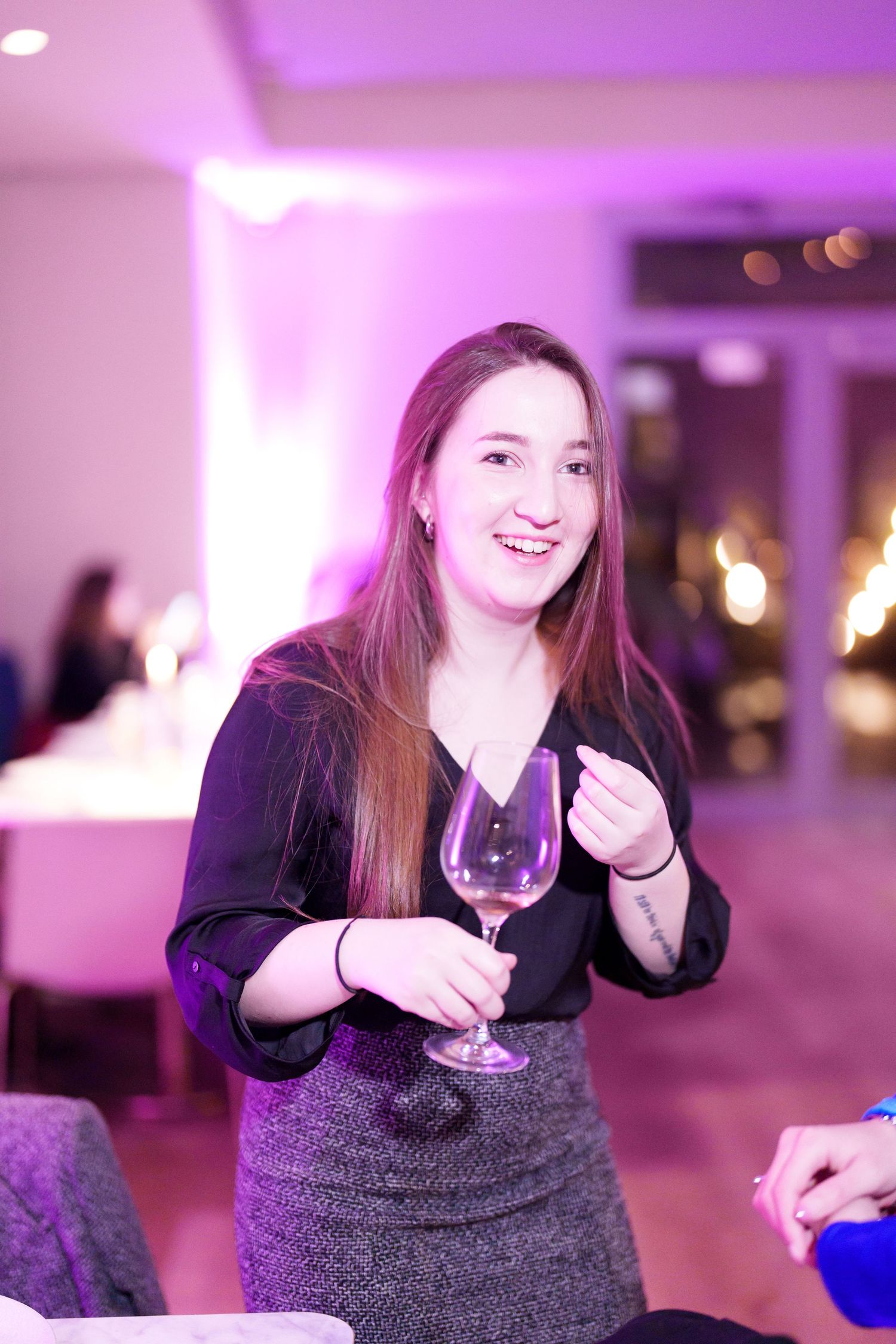 Smiling woman holding a wine glass at an elegant indoor event with purple ambient lighting.