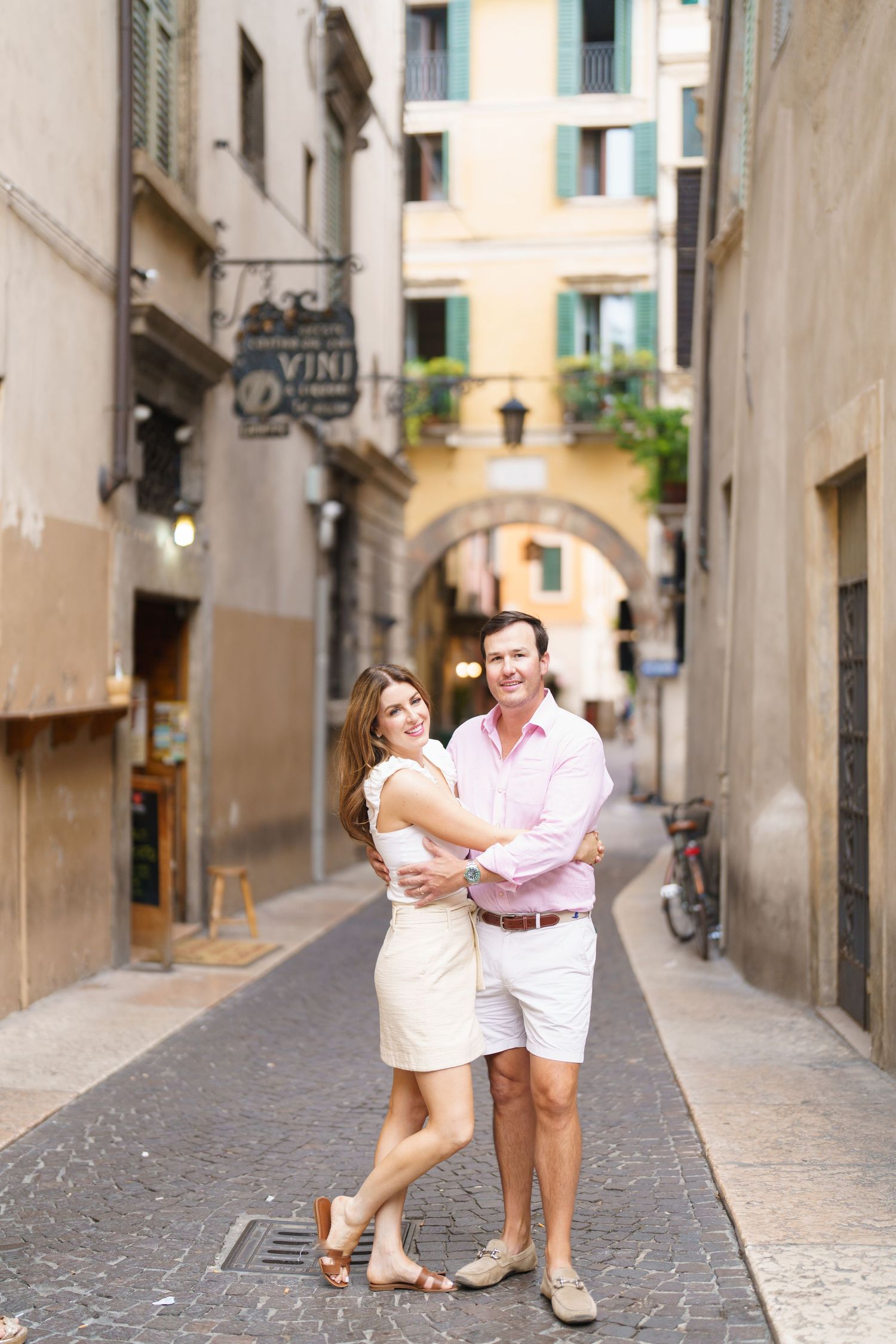 Couple embracing and smiling on a charming Italian cobblestone street with historic buildings and archway.